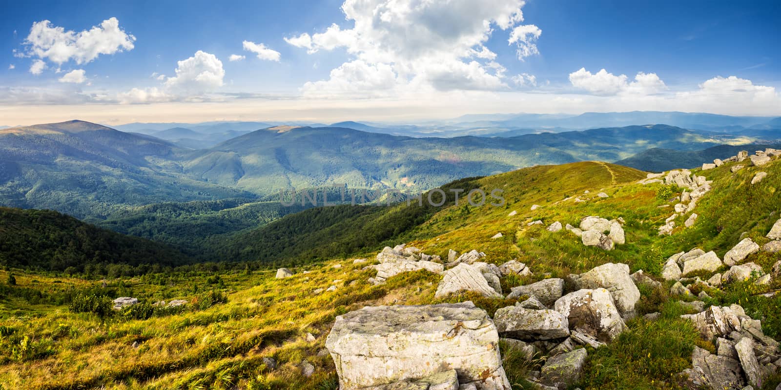mountain panorama landscape. valley with stones in grass on top of the hillside of mountain range in dappled light