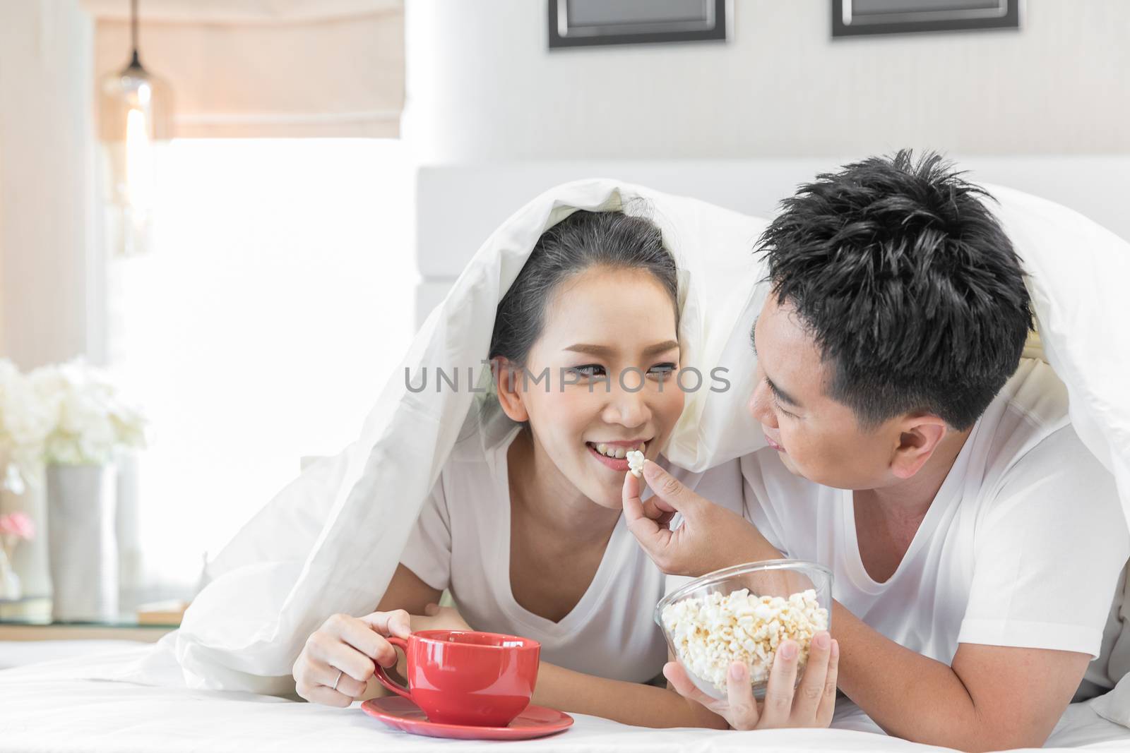 Young Asian Couples having breakfast on bed together in bedroom of contemporary house for modern lifestyle concept