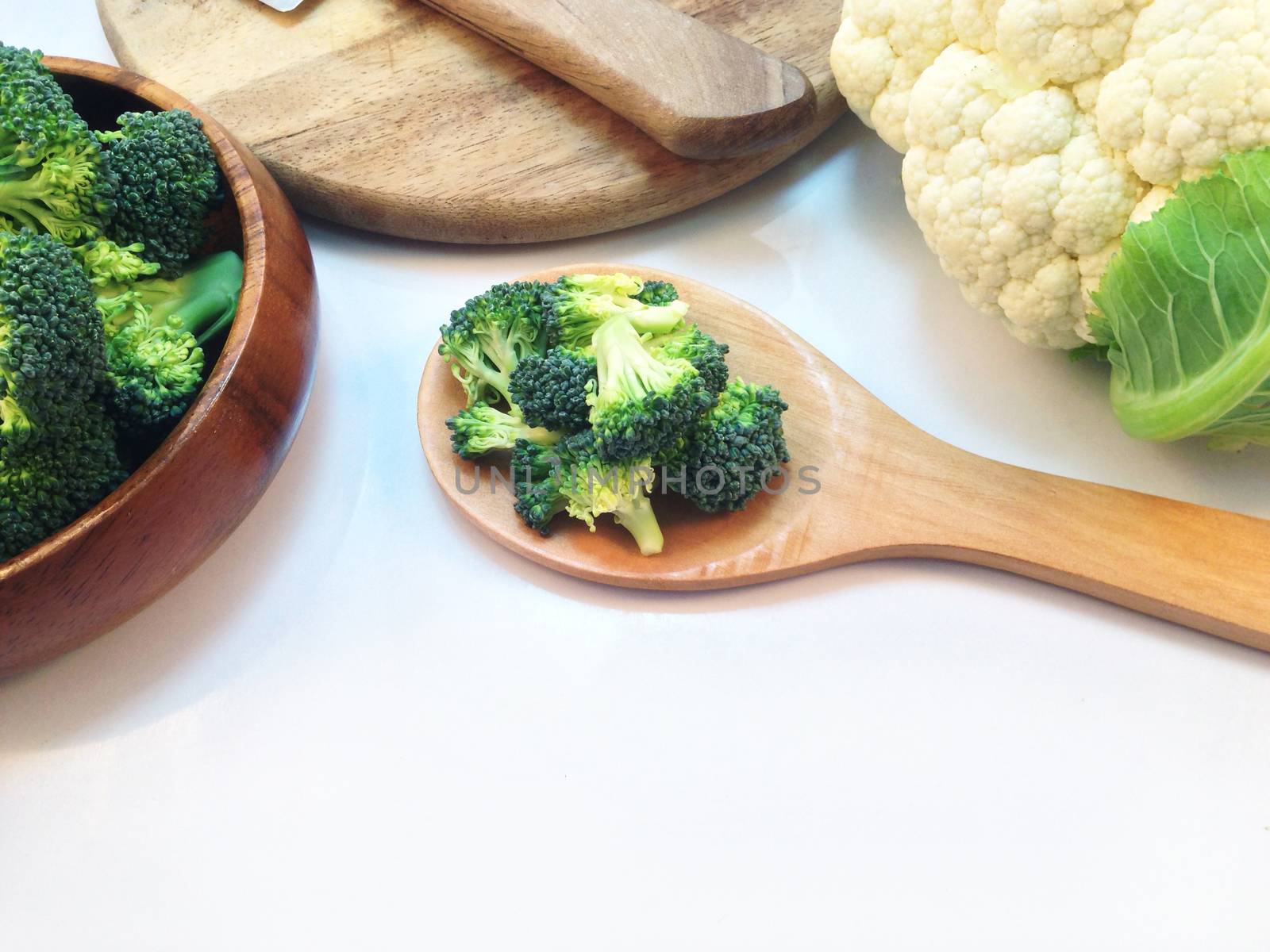 Broccoli in wooden bowl and wooden ladle with cauliflower on white background