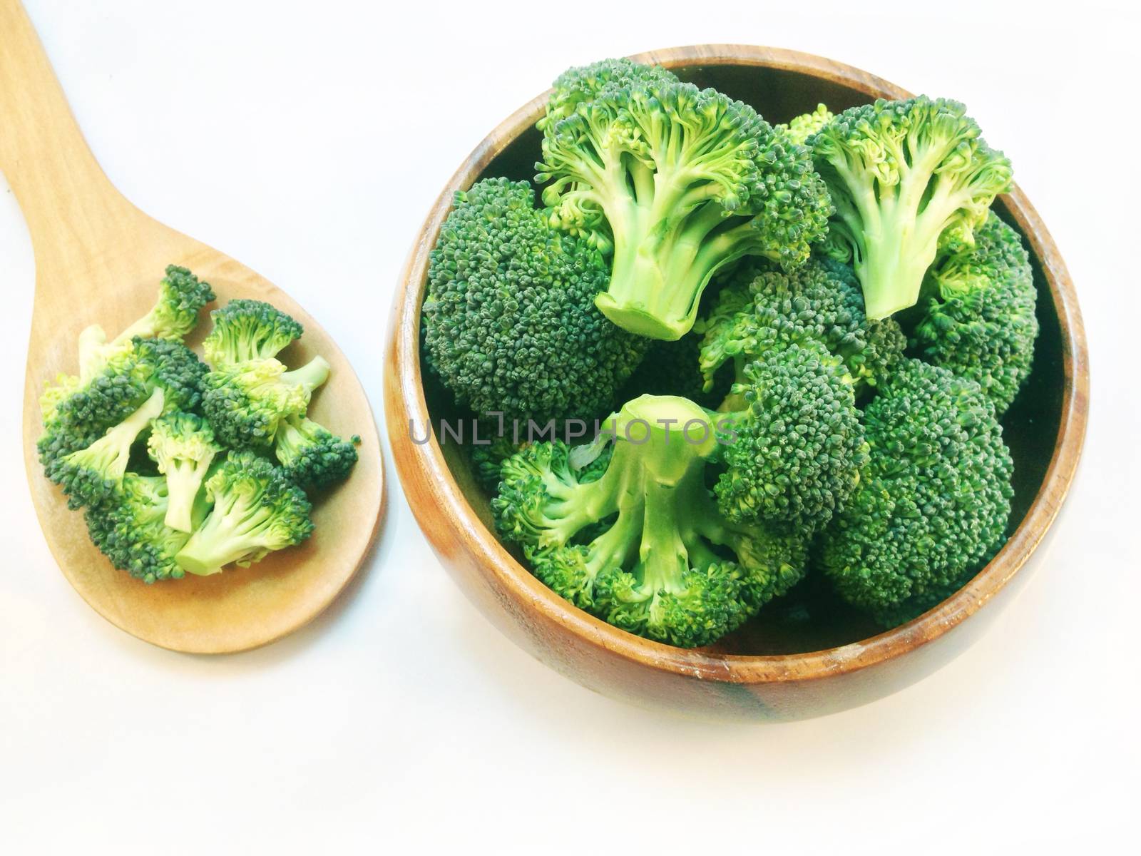 Broccoli in wooden bowl and wooden spoon on white background