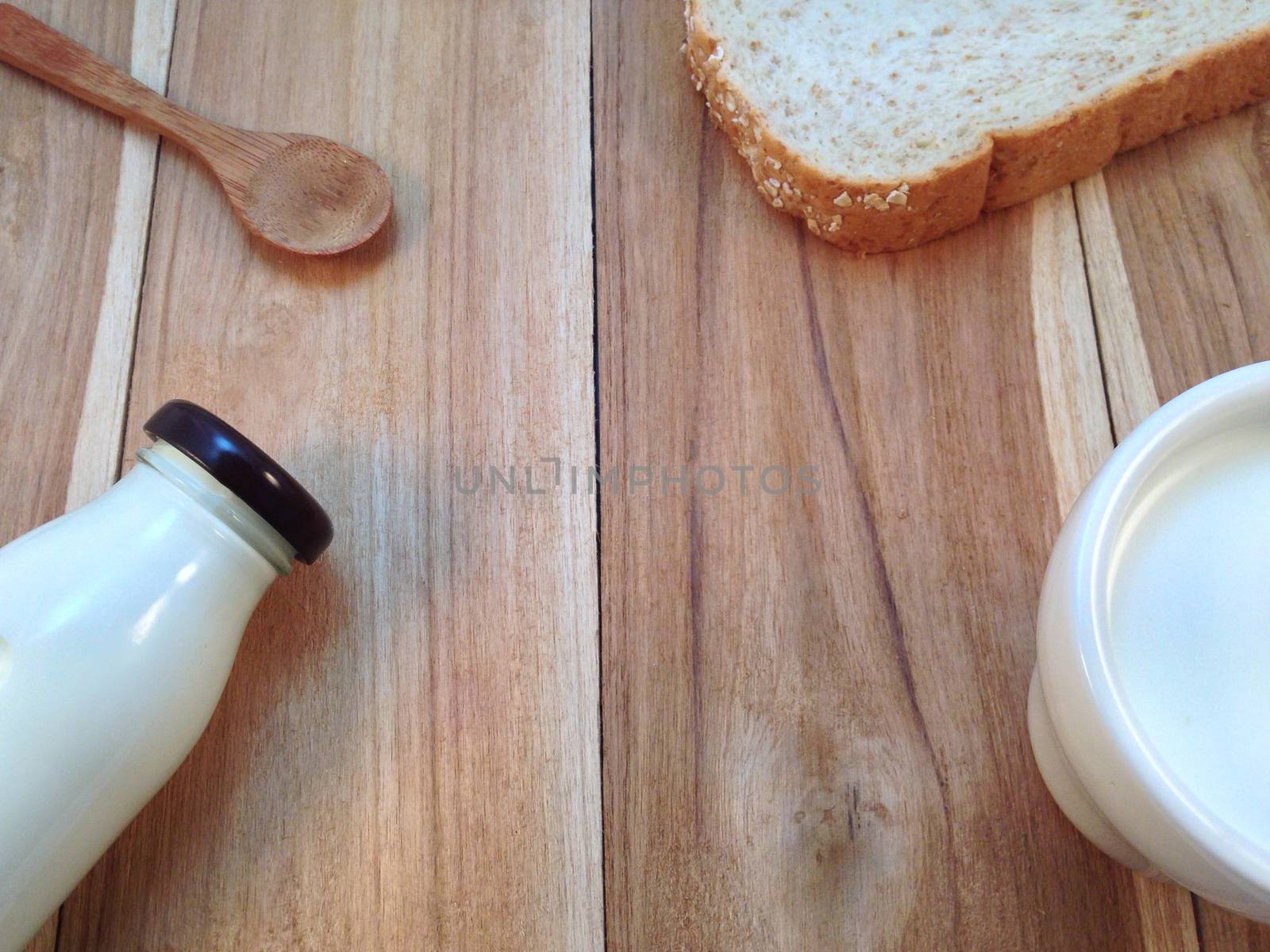 Slice of bread with bottle and cup of milk, wooden spoon on wooden background