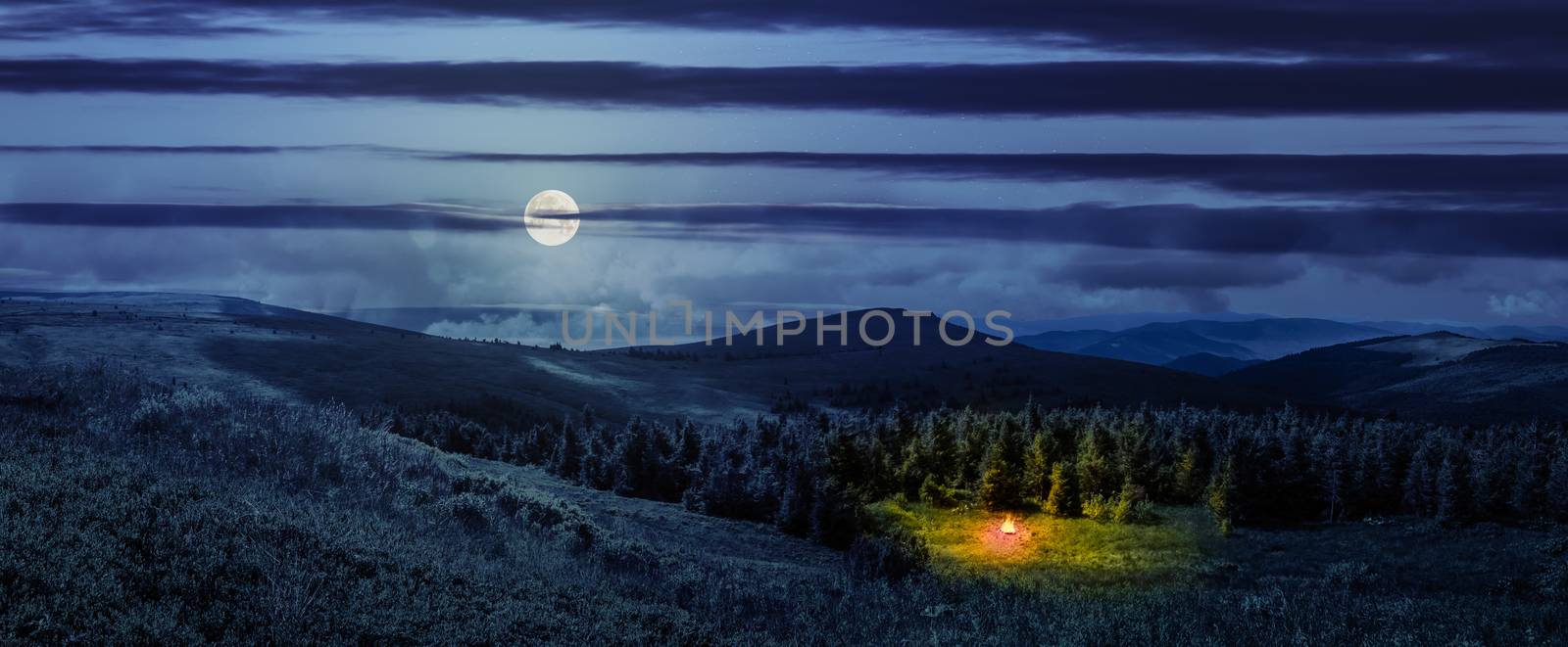 composite image of mountain range with bonfire in coniferous forest  on  hillside at night in full moon light