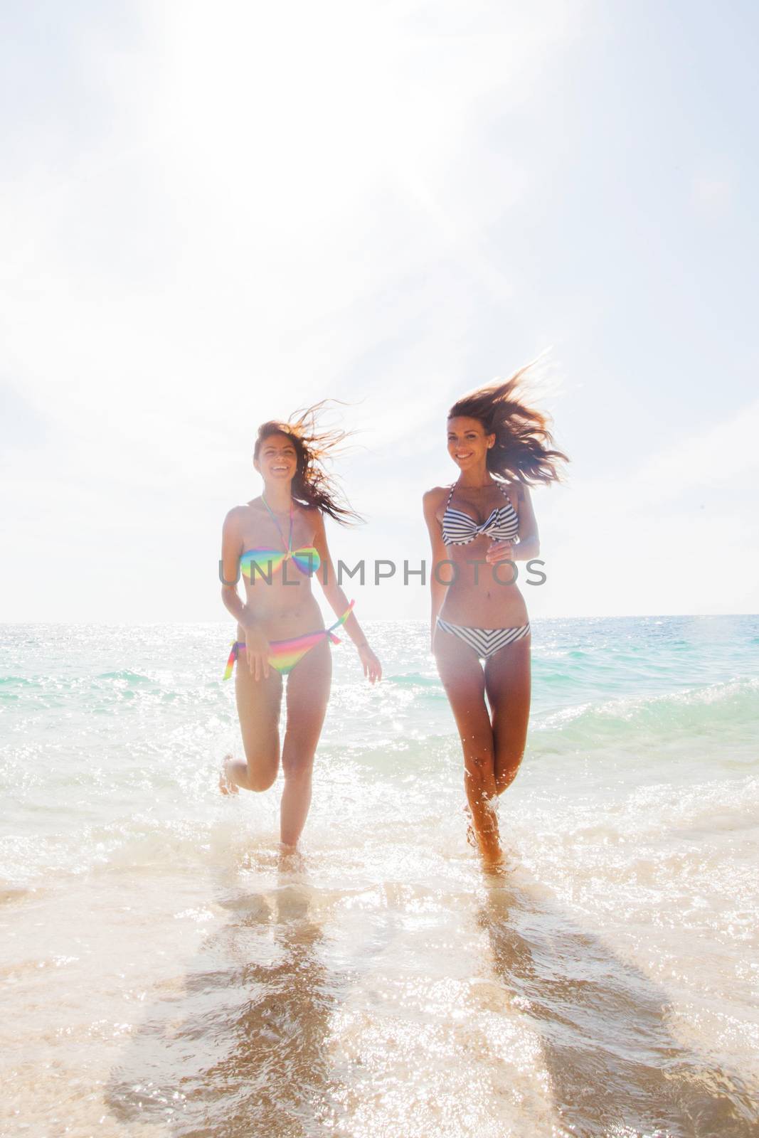 Two young and attractive women in bikini running by the beach