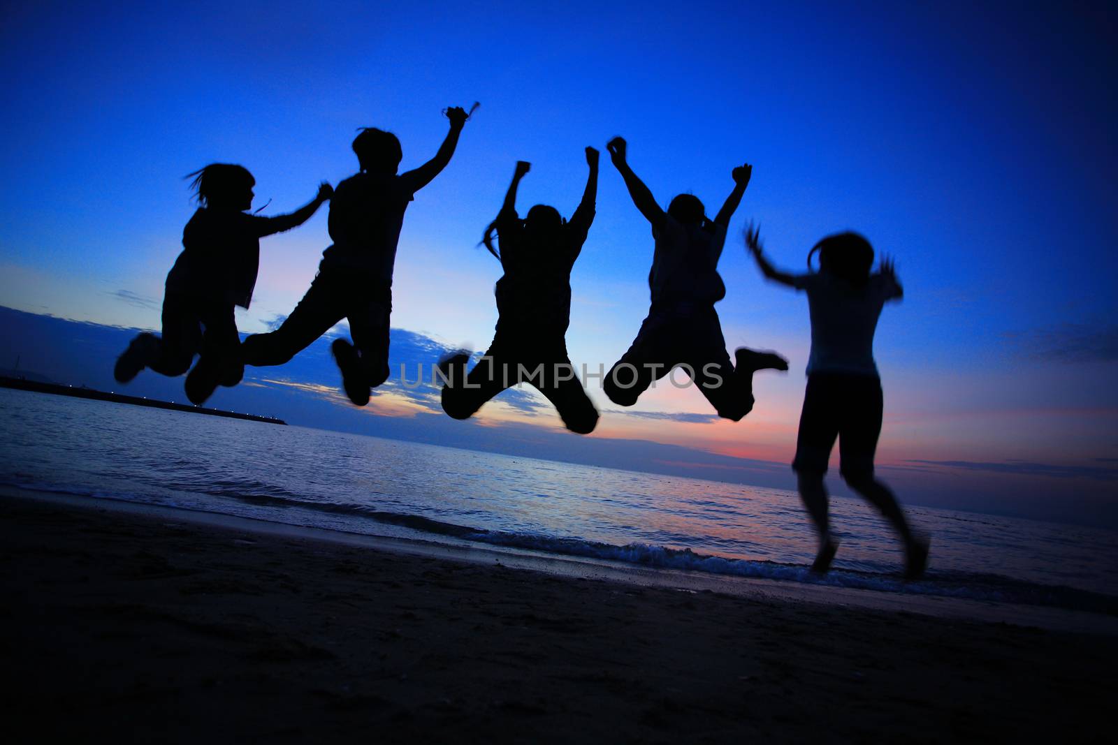 Silhouette of young friends jumping on the Pattaya beach and  backdrop of sunset over the sea in Thailand