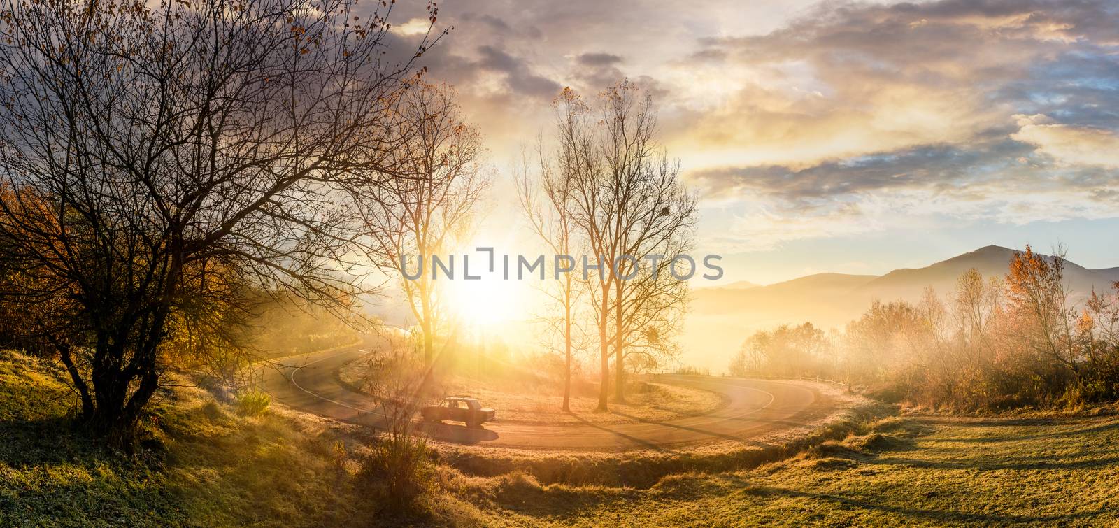 serpentine turnaround on foggy sunrise. naked trees on grassy hillsides under gorgeous cloudy sky over the mountain ridge in a distance. beautiful late autumn scenery