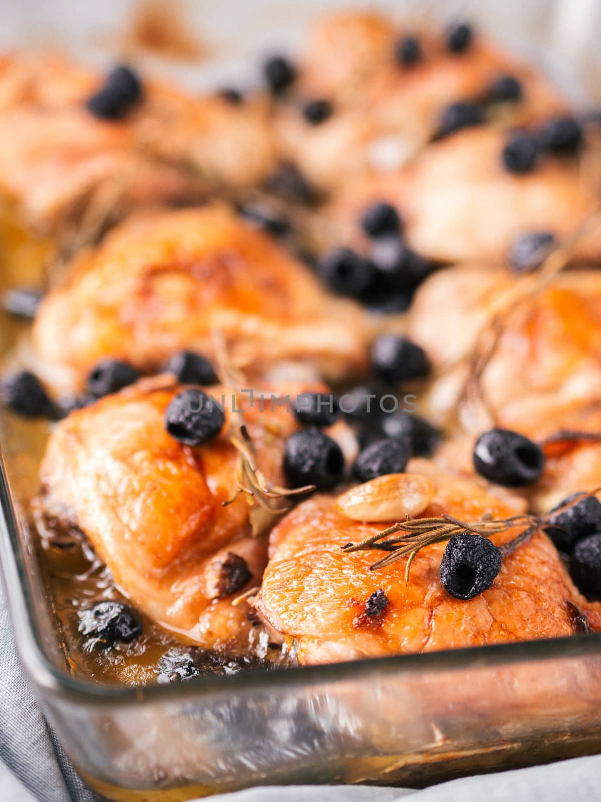 Corsican chicken thighs with rosemary, black olives, garlic in lemon juice and wine. Chicken legs cooked in oven on gray concrete background. Baked chicken leg in heat-proof glass. Copy space