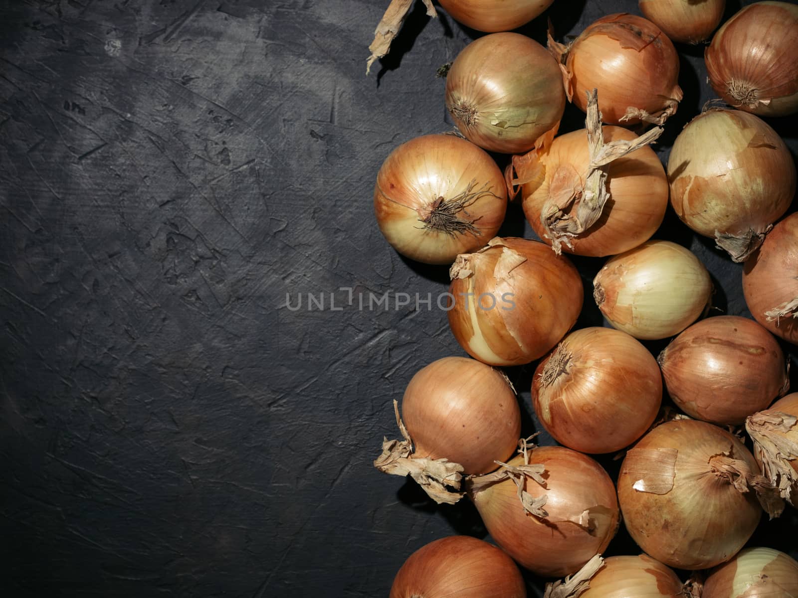 Fresh yellow onions on black concrete background. Onions with copy space. Fresh onions in low key. Hard light. Top view.