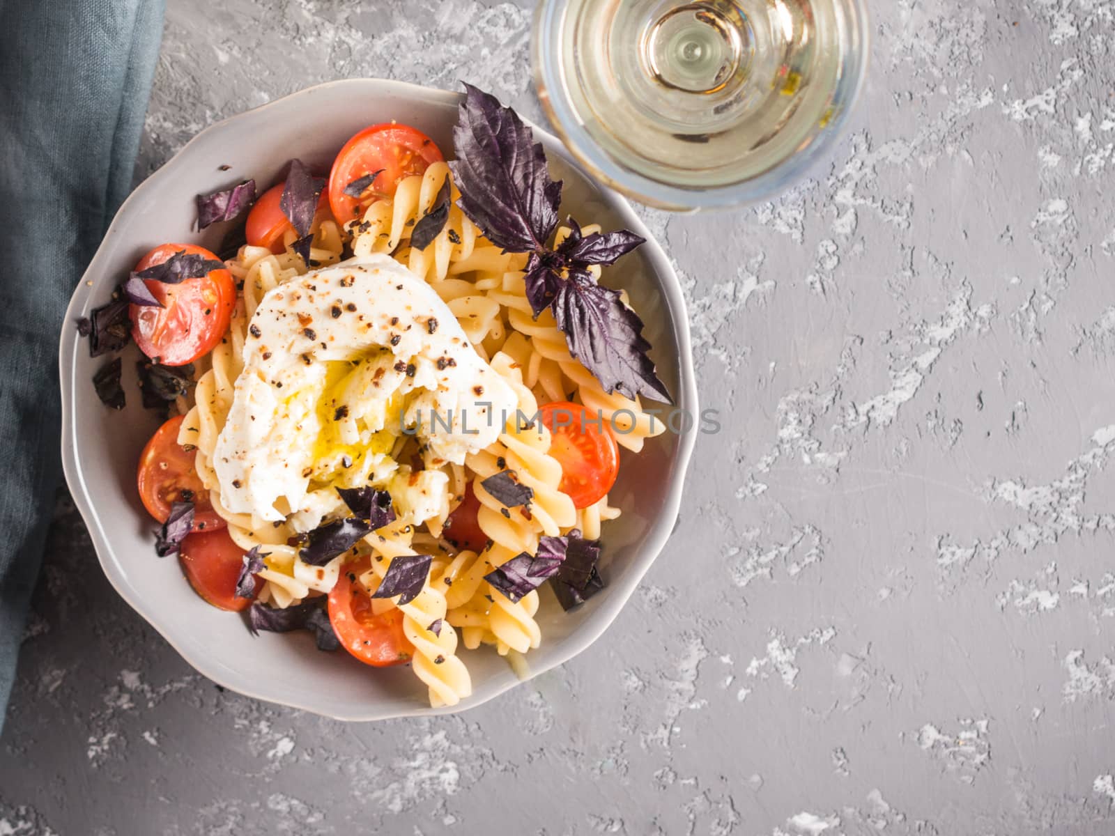 Tasty italian fusilli pasta with cherry, mozarella or buratta cheese and fresh basil. Dish with pasta on gray concrete background. Top view. Copy space. Healthy food concept and recipe idea.