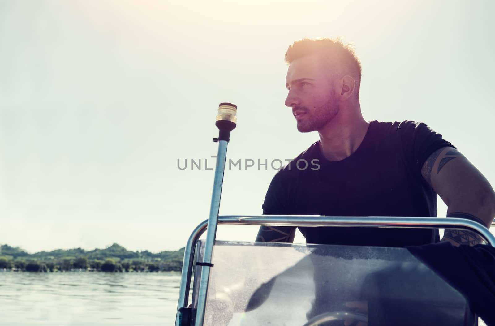 Young man sitting on yacht sailing on sea in back light.