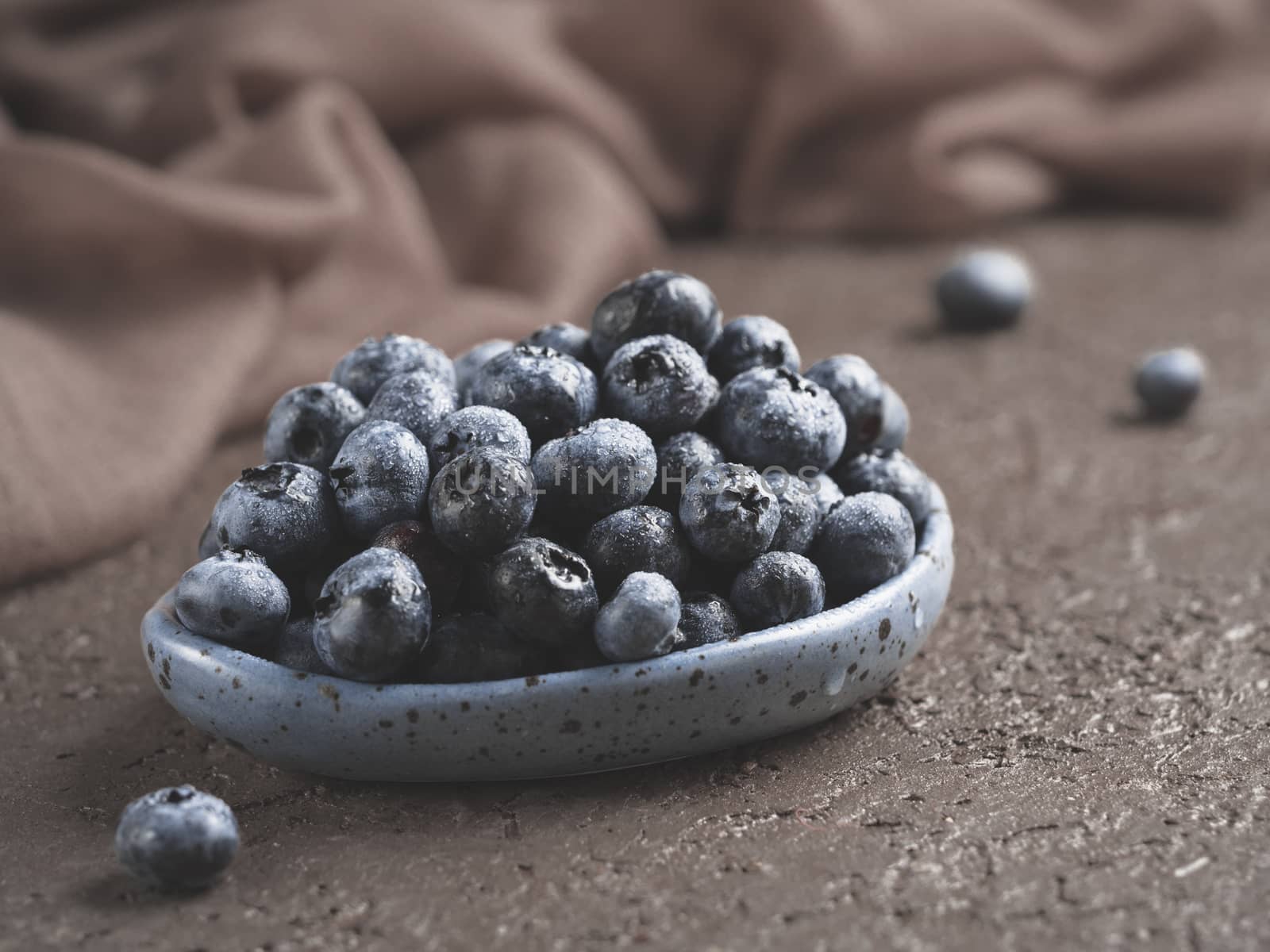 Blueberries in plate on brown concrete background. Fresh picked bilberries close up. Copyspace. Close up