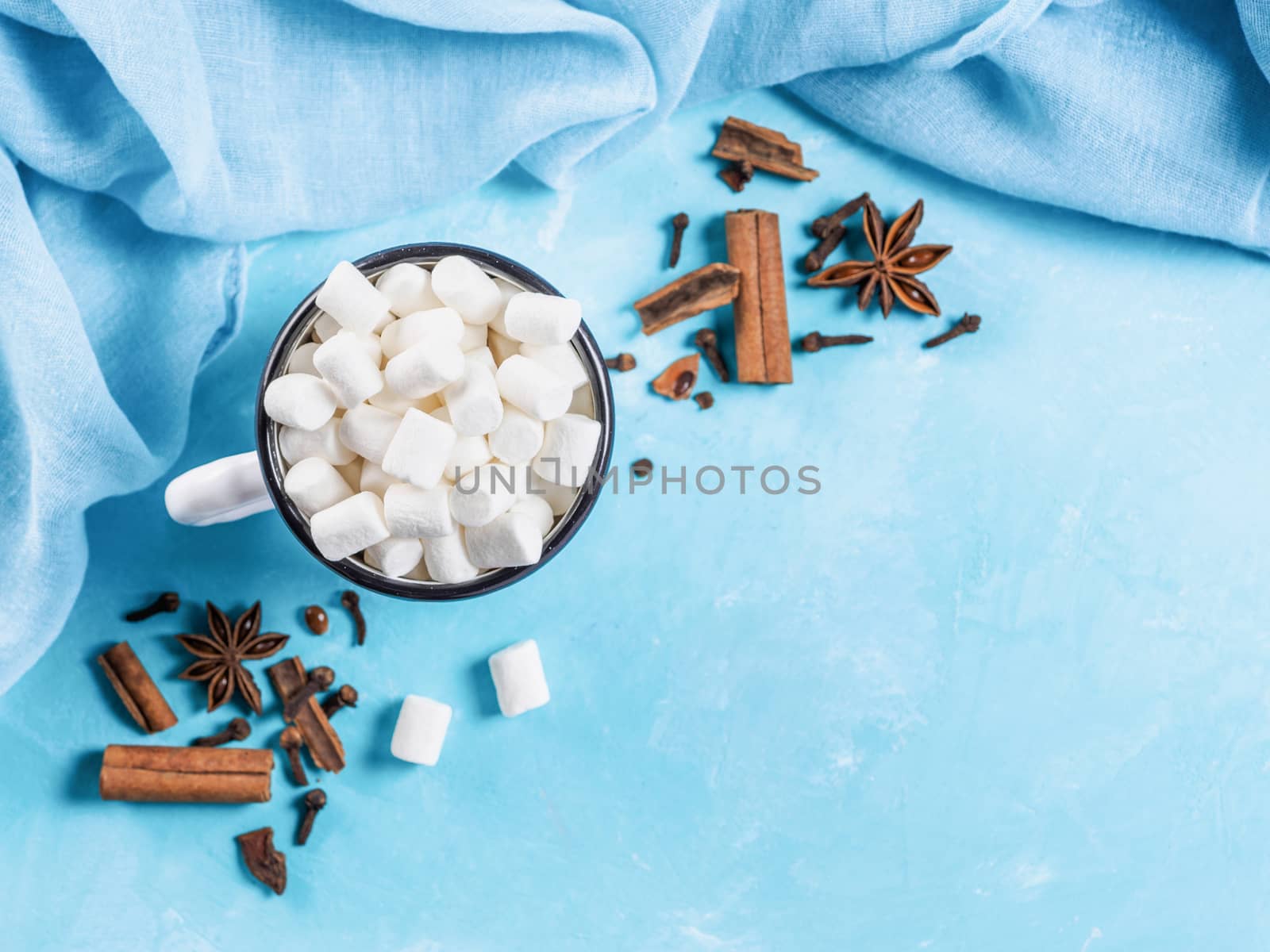 Marshmallows and winter spices on blue background with copyspace. Flat lay or top view. Background of colorful mini marshmallows, cinnamon, cloves and star anise. Winter food background concept.