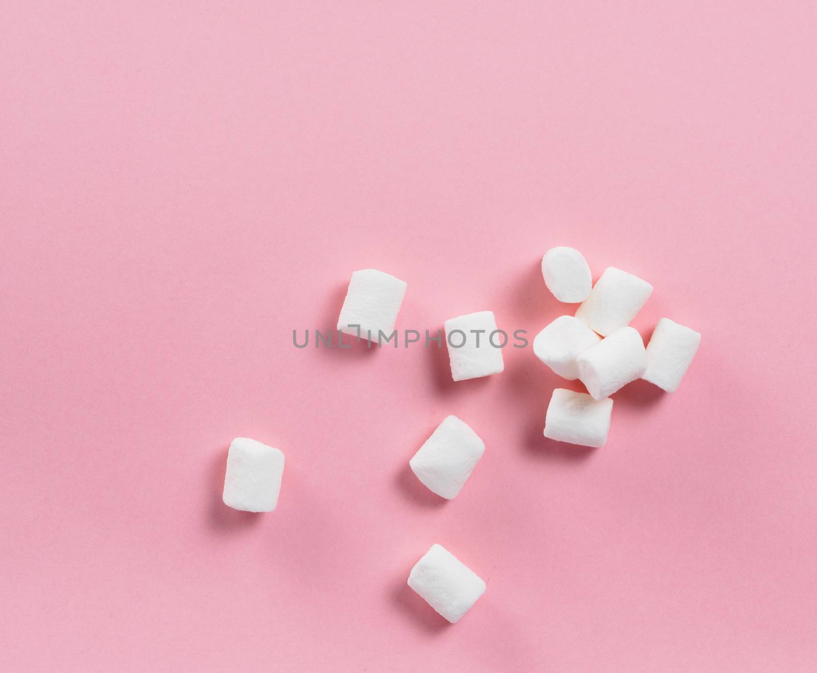 Marshmallows on pink background with copyspace. Flat lay or top view. Background or texture of colorful mini marshmallows. Winter food background concept.