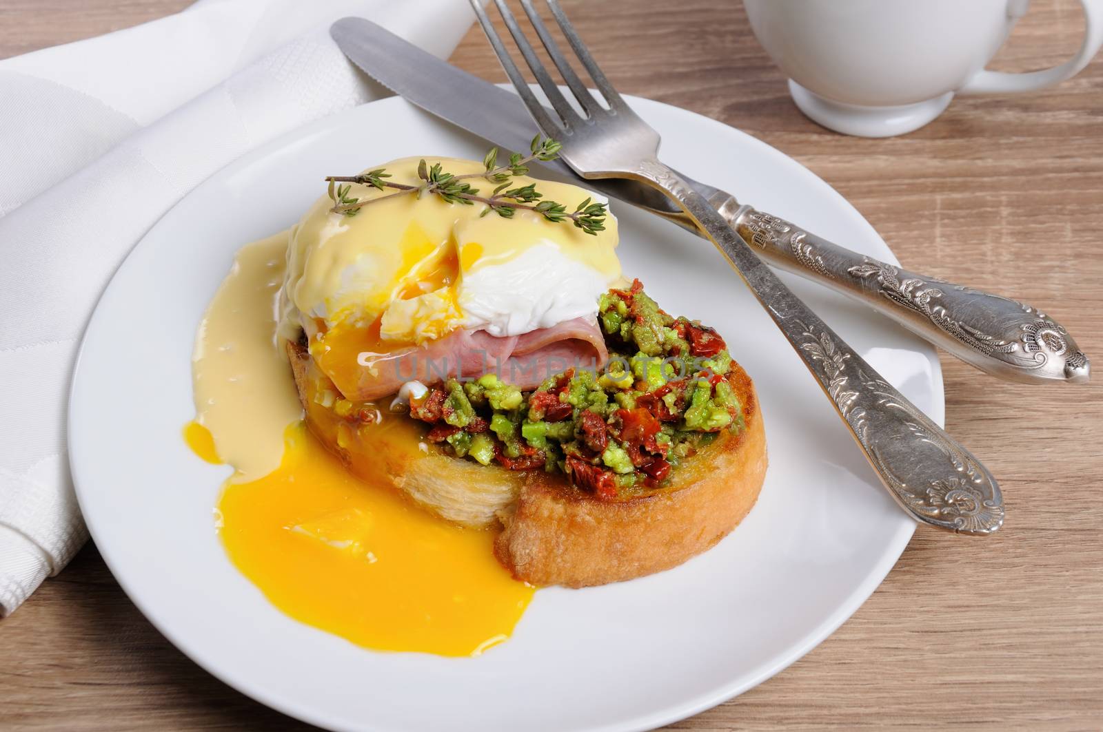 Toasted baguette slice with guacamole, ham and eggs Benedict under Dutch sauce