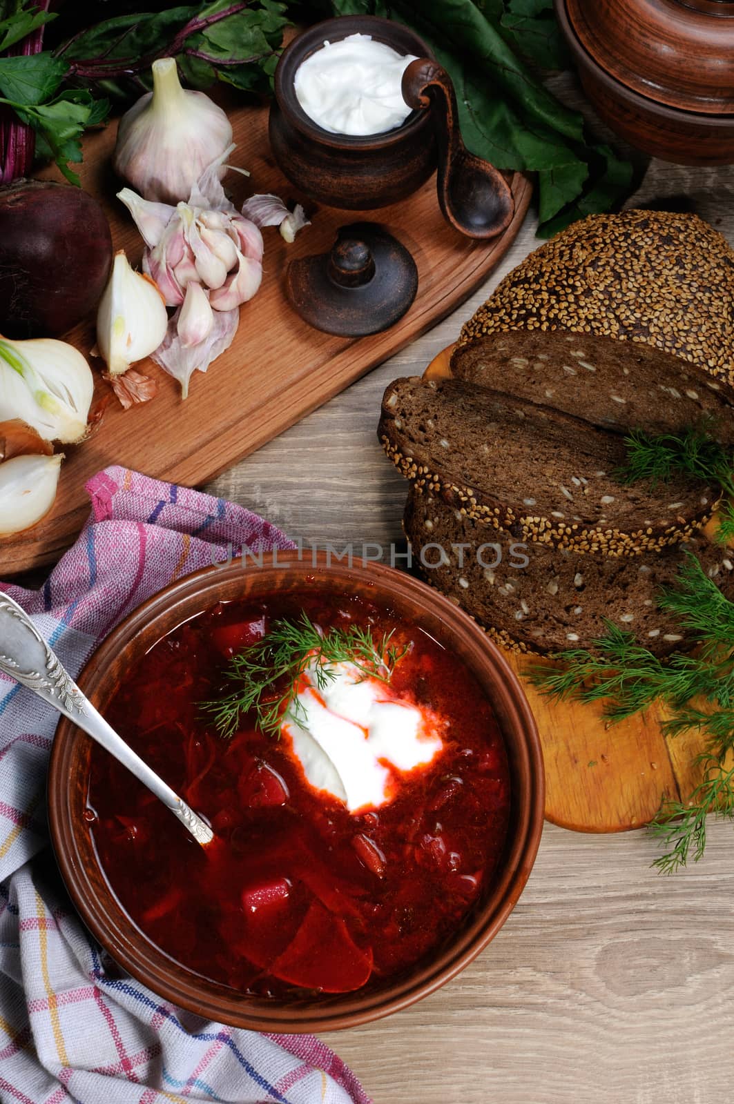 Borscht-vegetable beetroot soup, on the table with slices of rye cereal bread and gluten of sour cream, garlic and herbs. Rustic style.