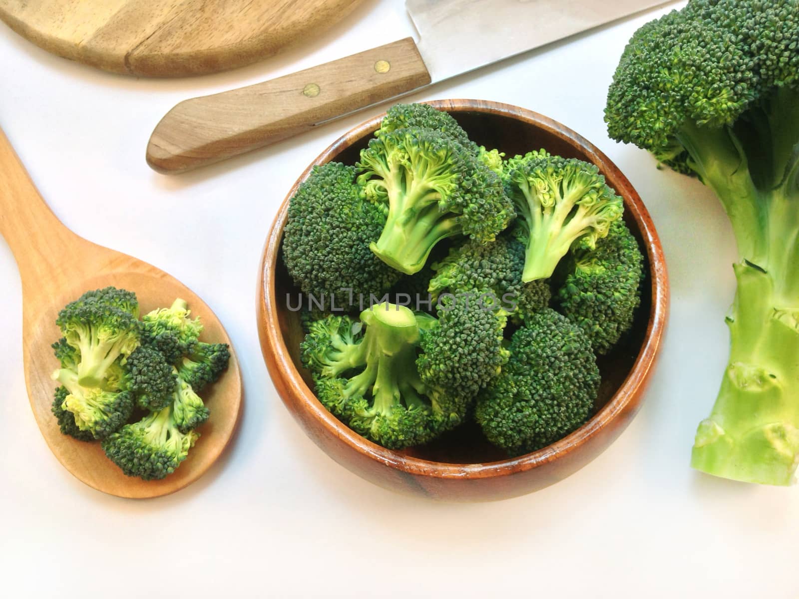 Broccoli on wooden ladle and wooden bowl, cutting board, knife on white background