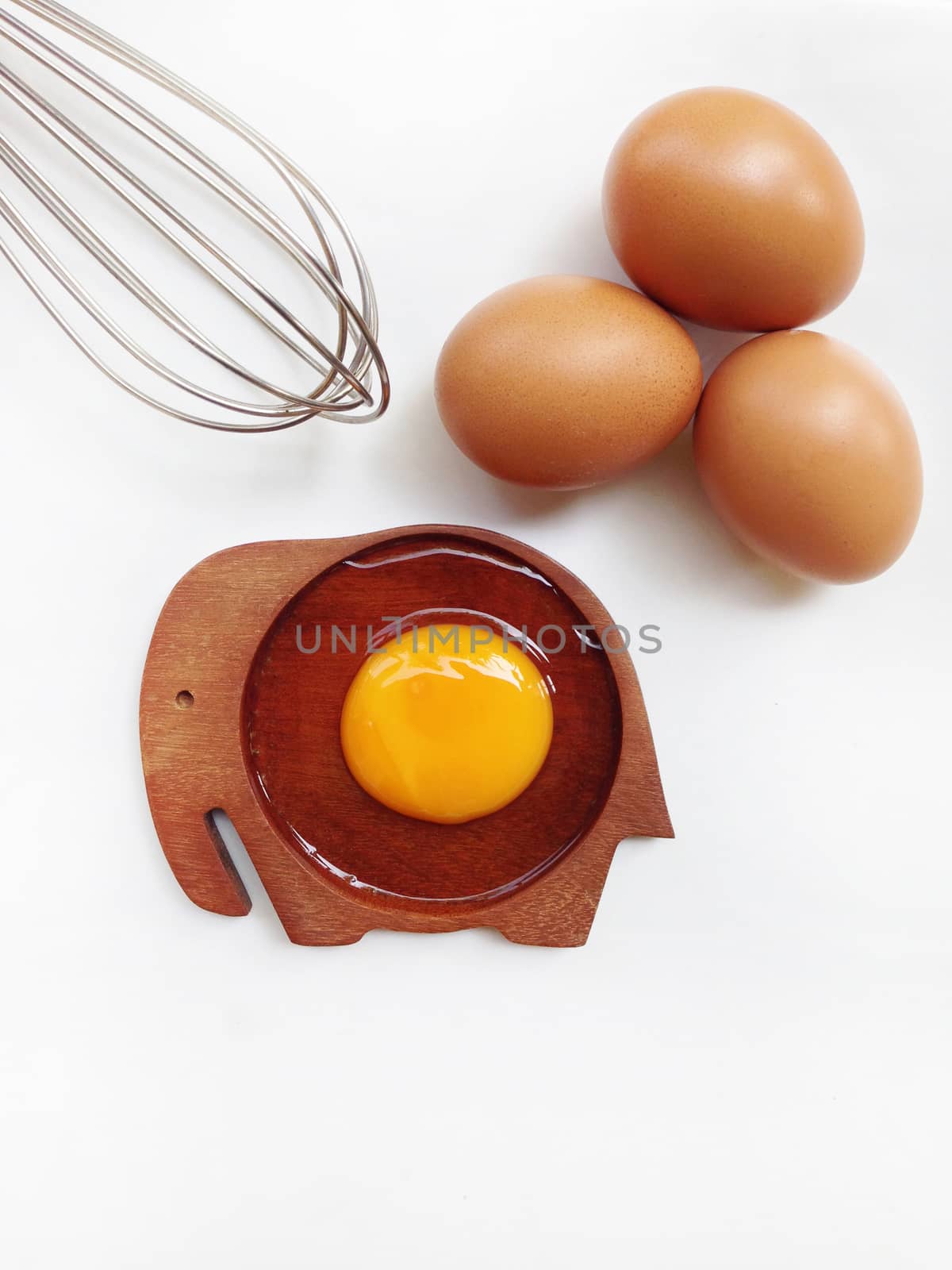 Egg yolk on wooden elephant shaped saucer with eggs and egg whisk on white background