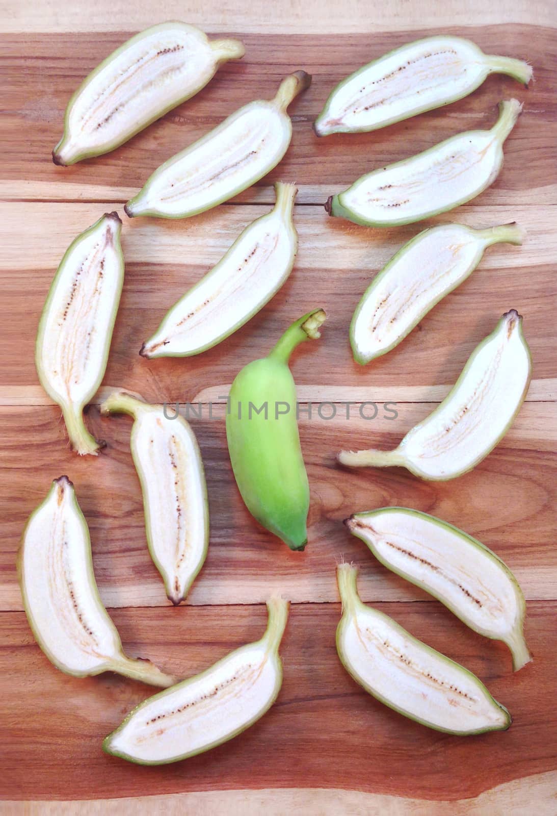 Green cultivated banana and piece of slices on wooden background by Bowonpat