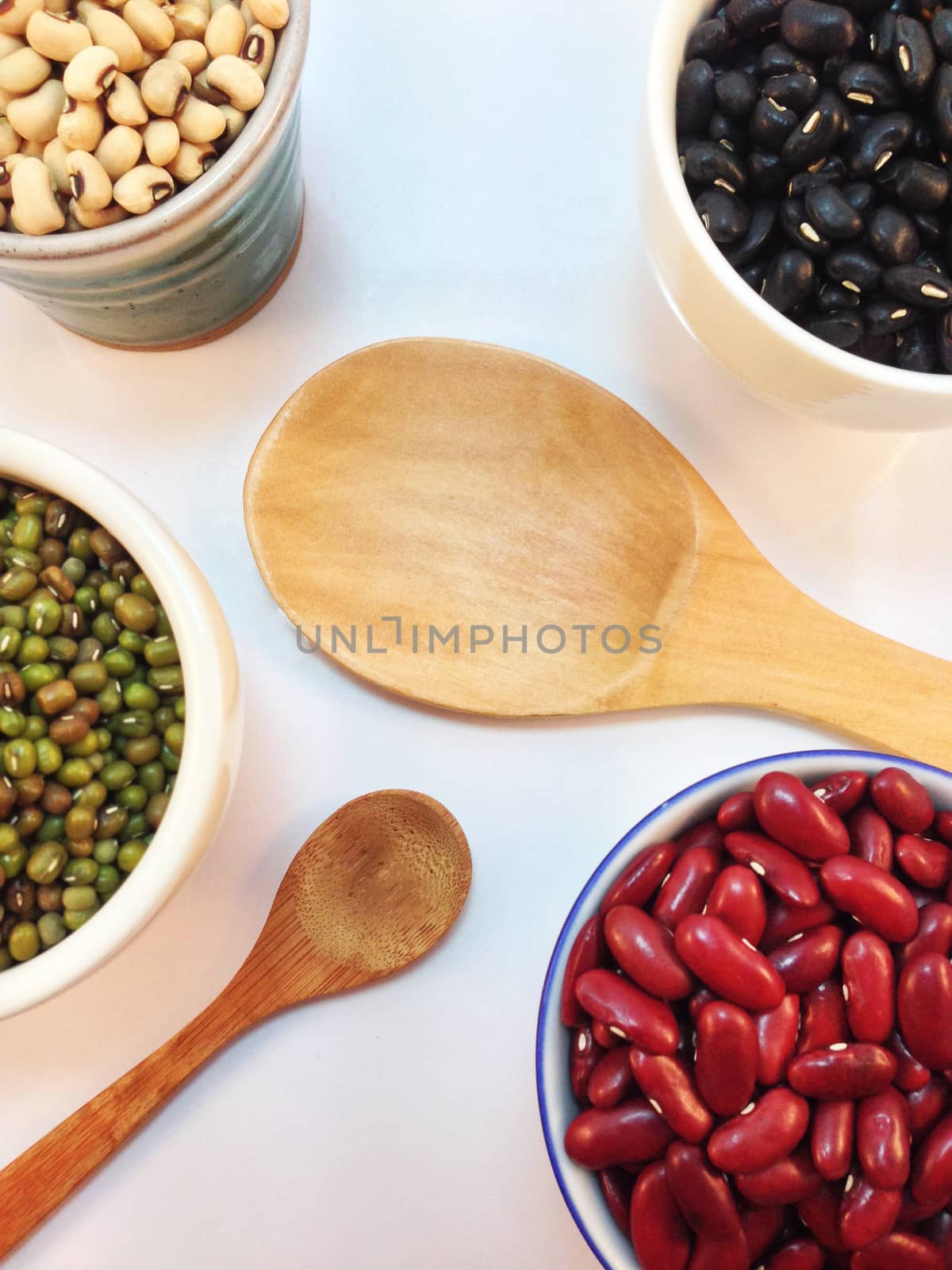 Black eye peas, mung beans, black beans and red kidney beans in a cup with wooden spoon and wooden ladle on white background