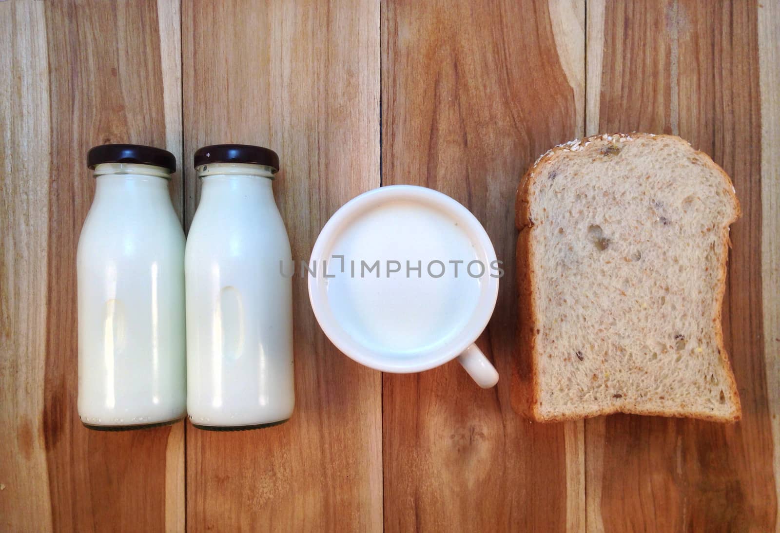 Slice of bread with bottle and cup of milk on wooden background