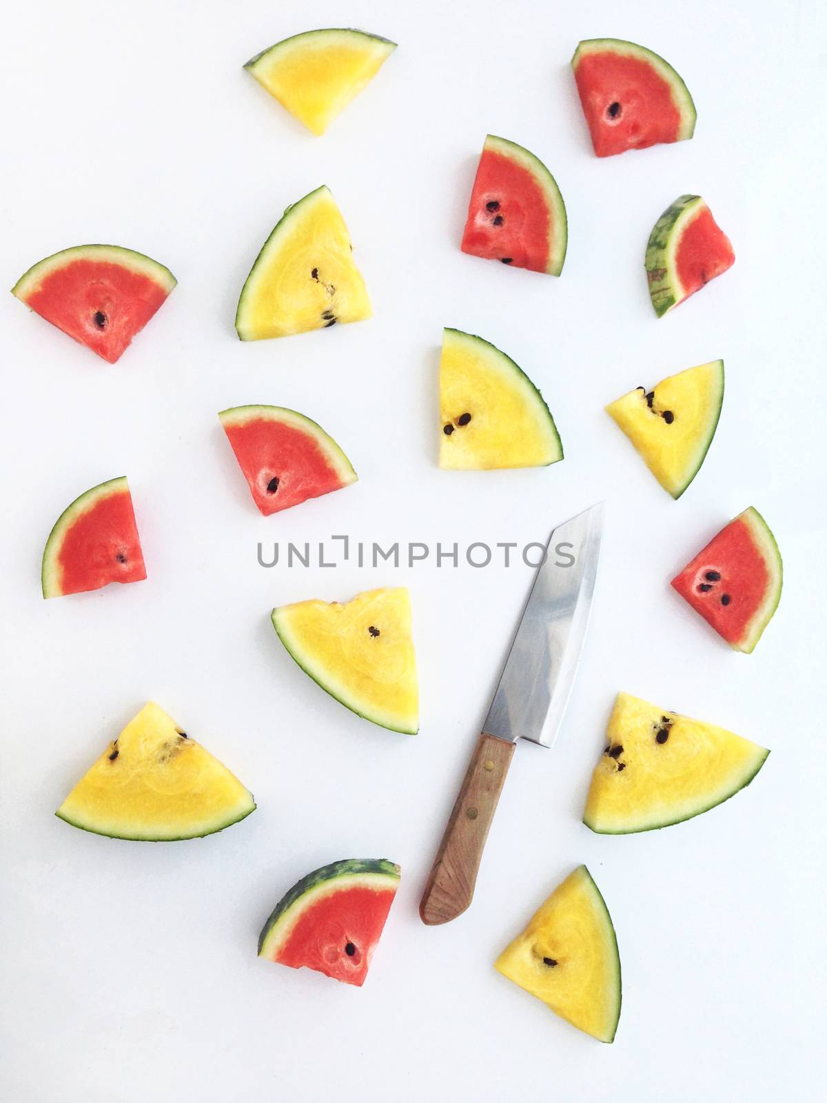 slices of red and yellow watermelon and knife on white background