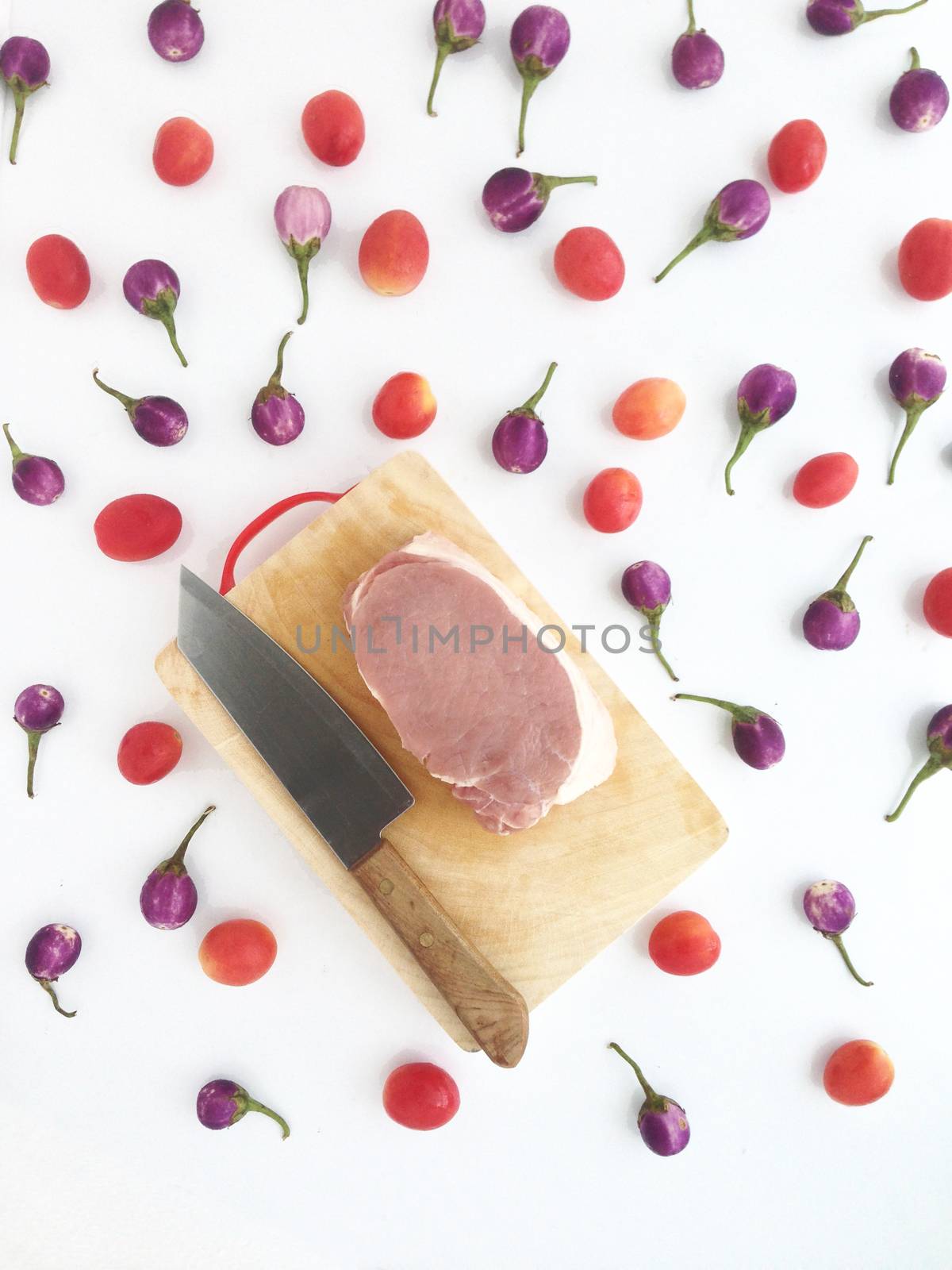 Pork on cutting board with tomatoes and  Thai eggplants