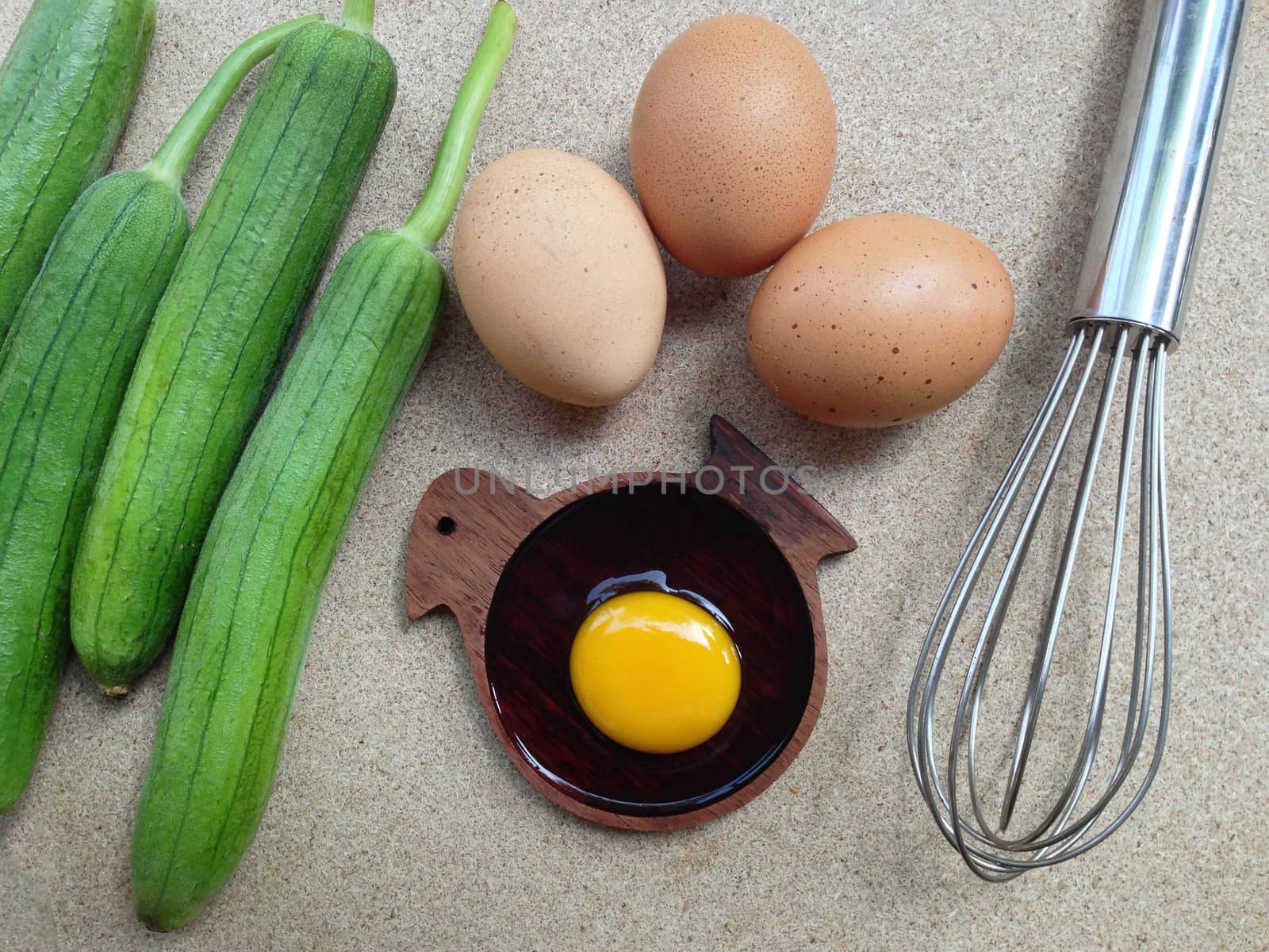 Yolk egg on wooden elephant shaped saucer with eggs, angle gourd and egg whisk on plywood background