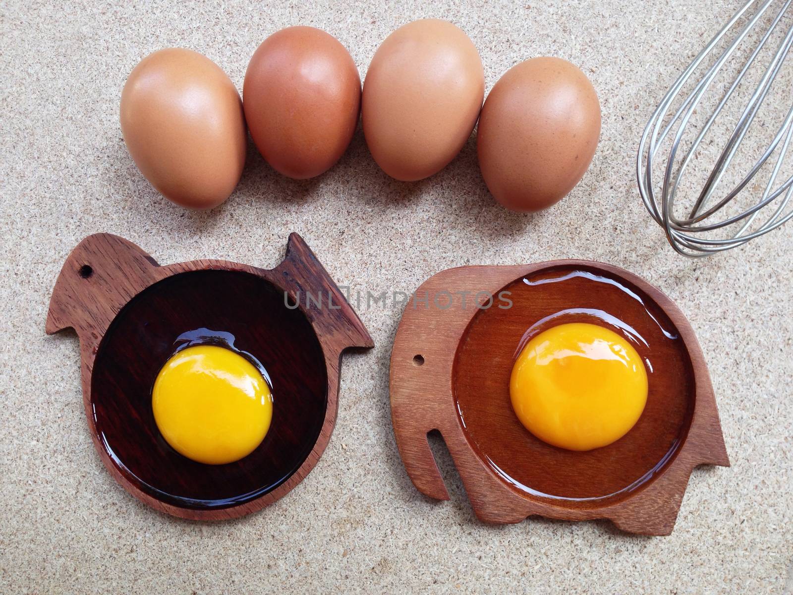 Egg yolk on wooden chicken shaped saucer and yolk egg on wooden elephant shaped saucer with eggs and egg whisk on plywood
