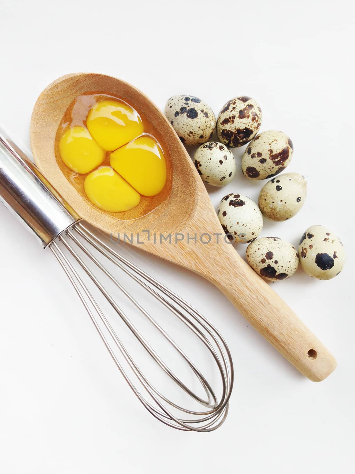 Quail eggs in wooden spoon and egg whisk on white background