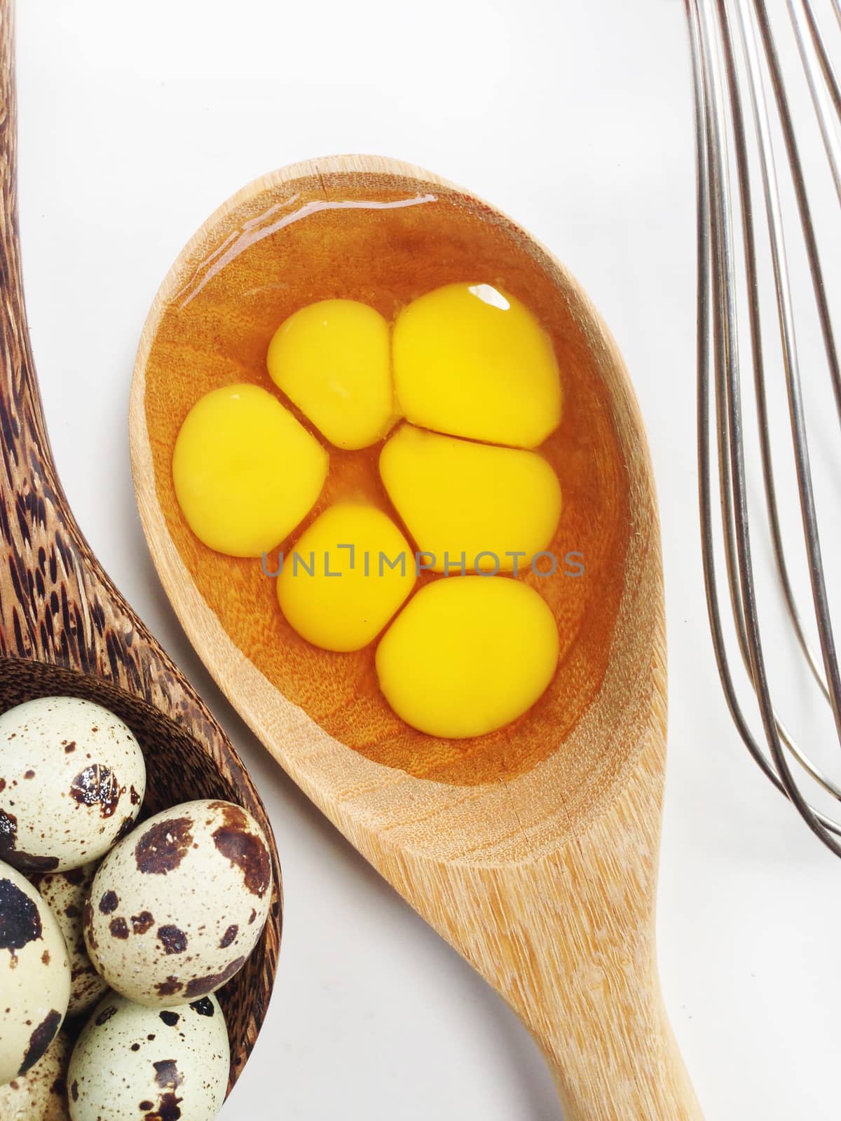 Quail eggs in wooden spoon and egg whisk on white background