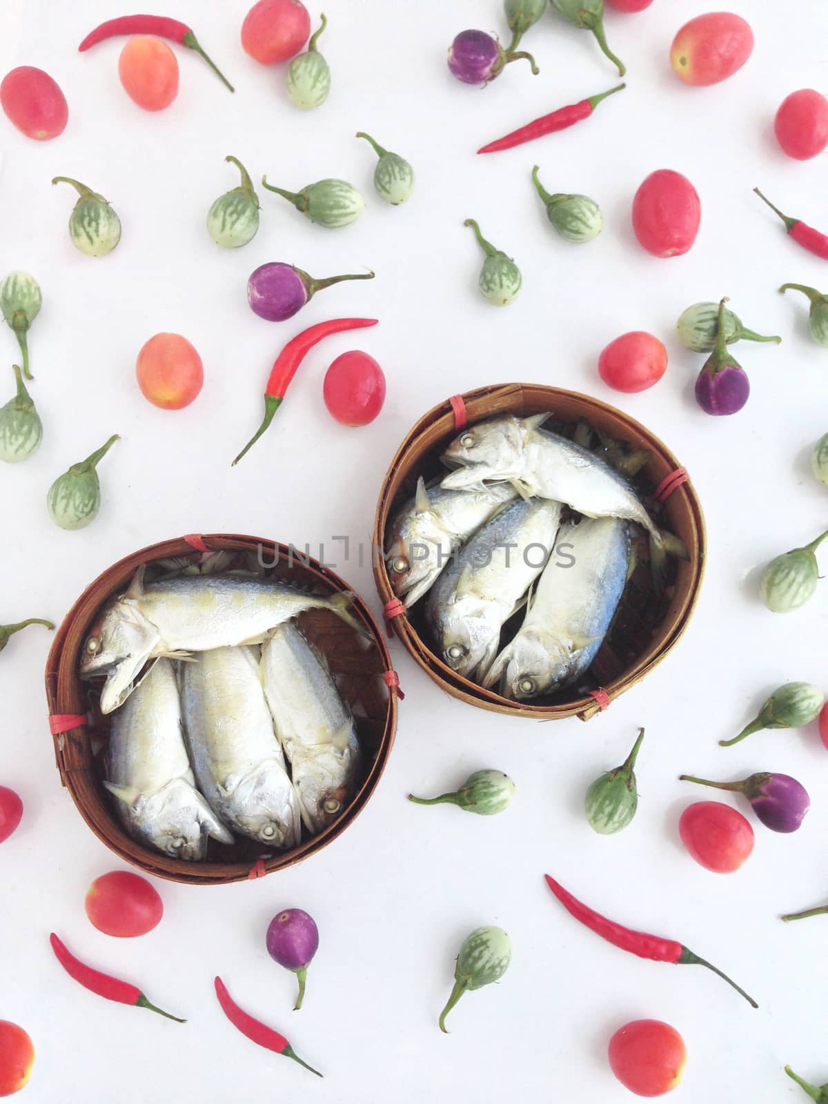 short mackerel on a round crate made of bamboo, used to transport fruits or fish, among vegetables