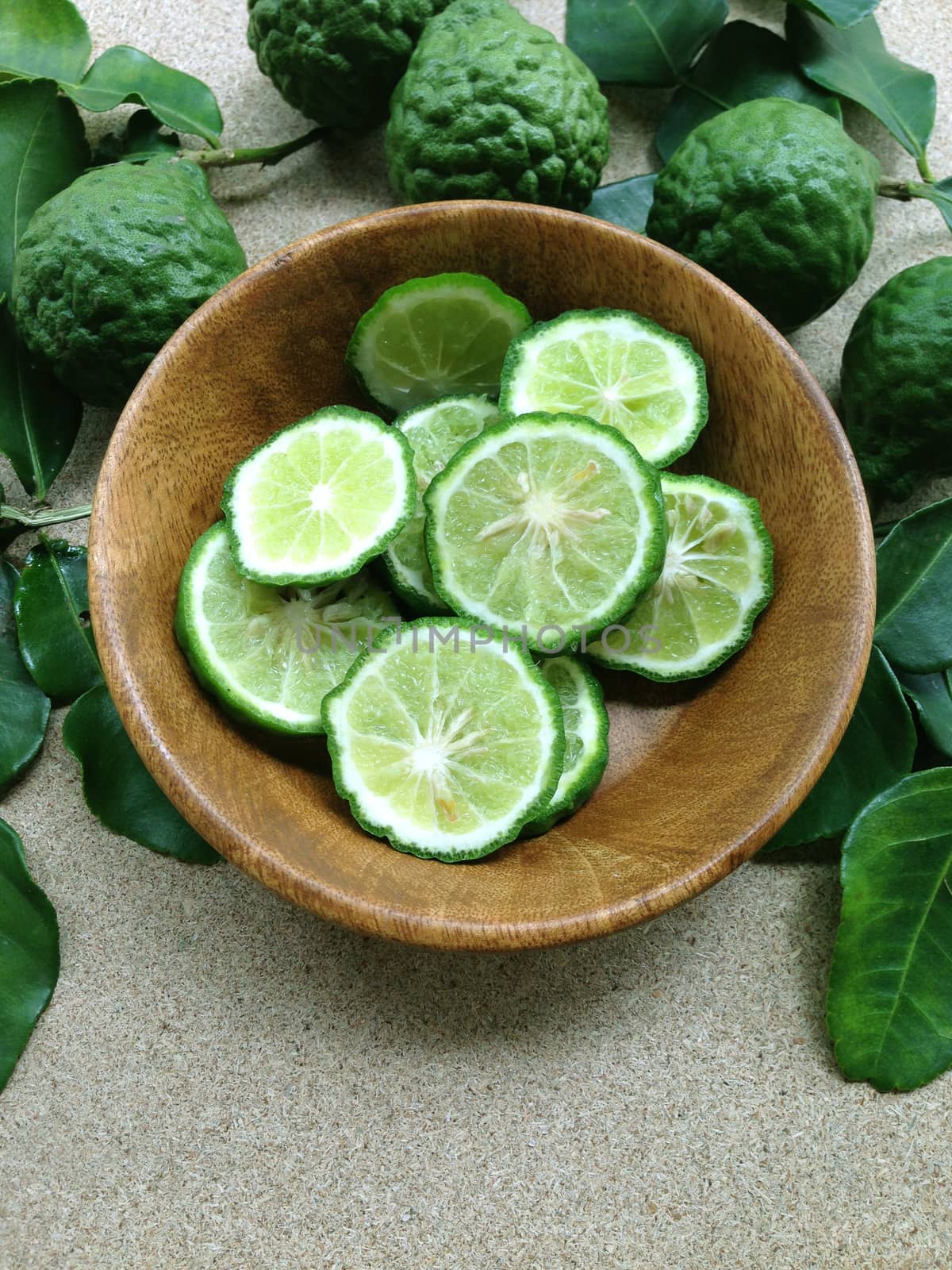 Kaffir Lime or Bergamot in wooden bowl on plywood background  by Bowonpat