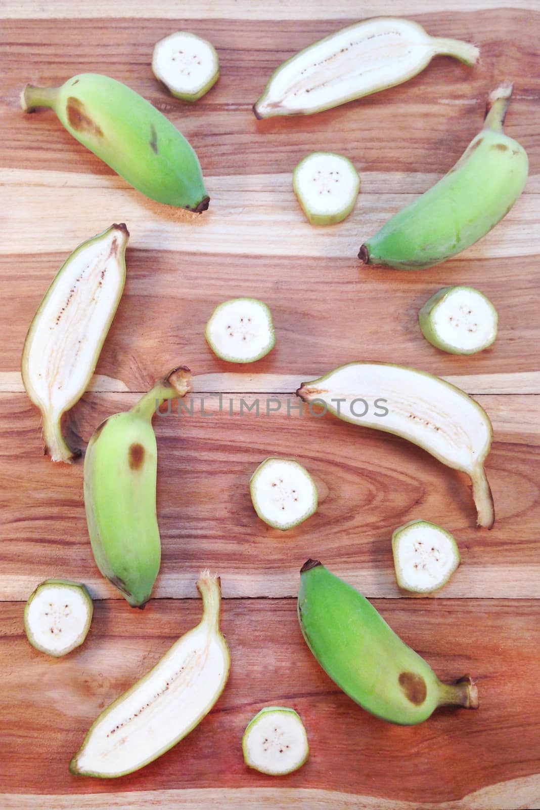 Green cultivated banana and piece of slices on wooden background by Bowonpat