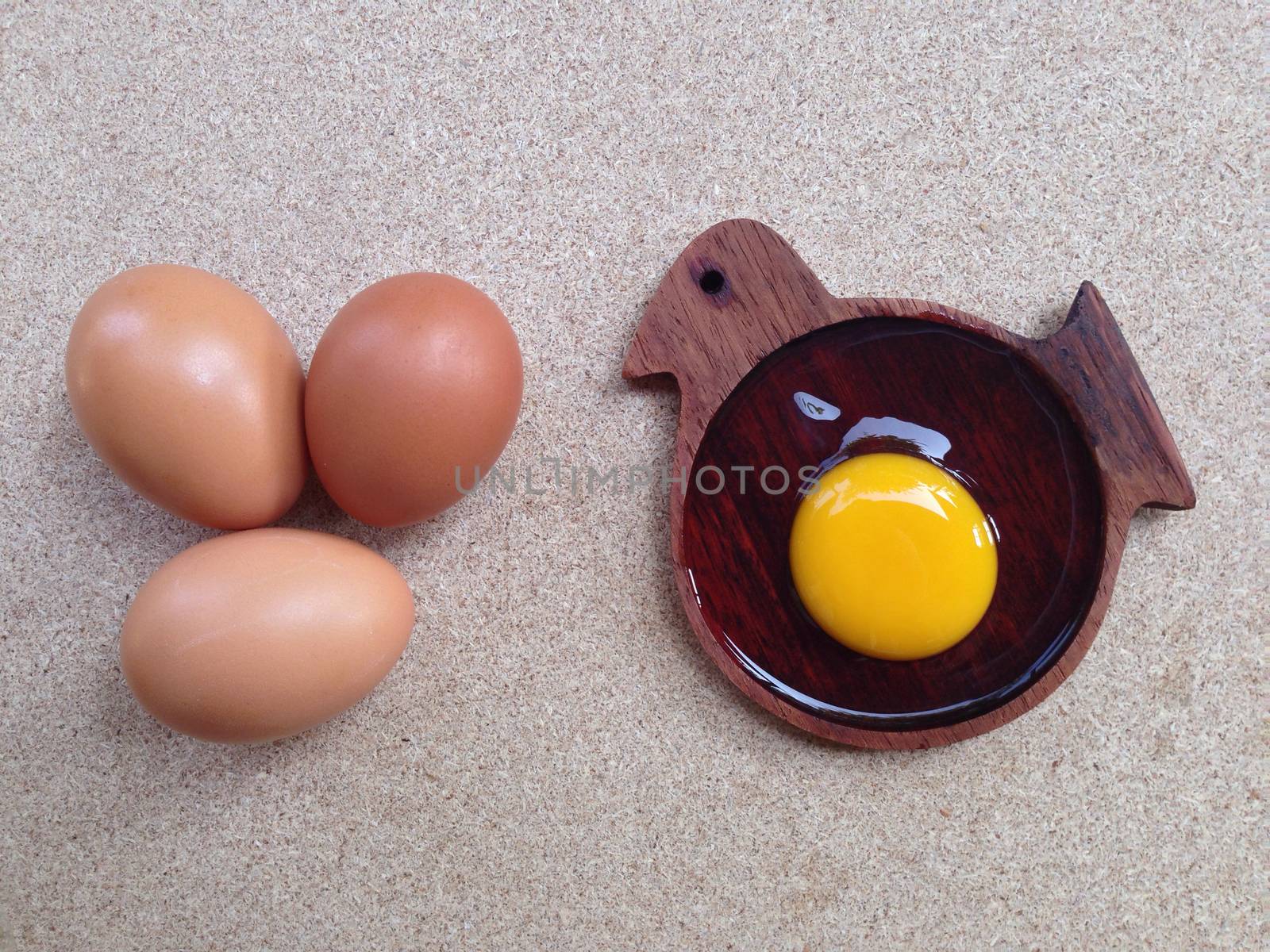 Egg yolk on wooden chicken shaped saucer and eggs on plywood by Bowonpat