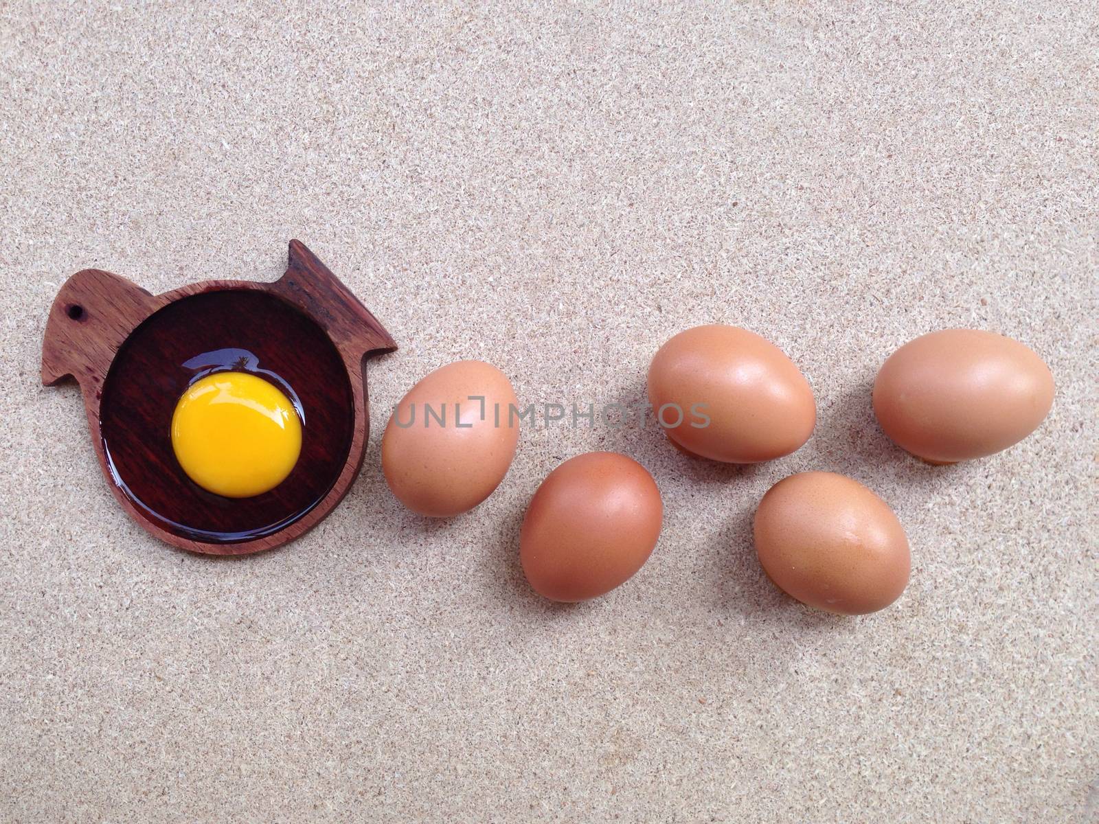 Egg yolk on wooden chicken shaped saucer and eggs on plywood by Bowonpat