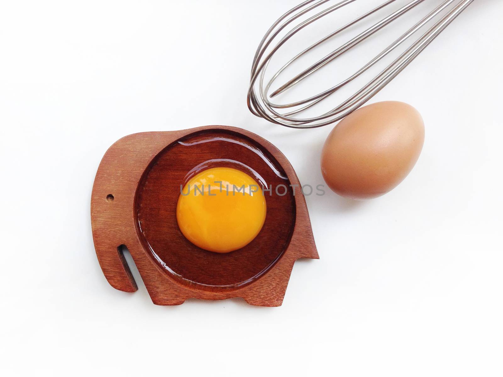 Egg yolk on wooden elephant shaped saucer with eggs and egg whisk on white background