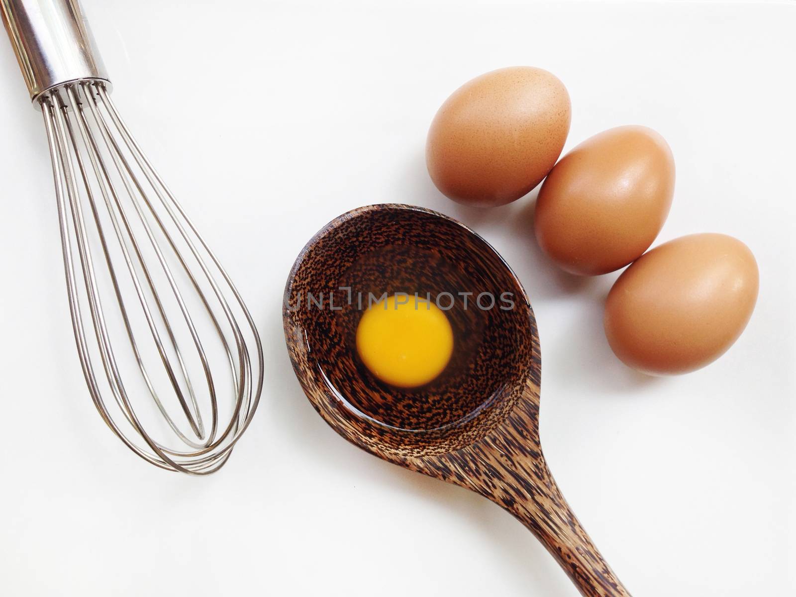 Egg yolk on wooden spoon and egg whisk on white background