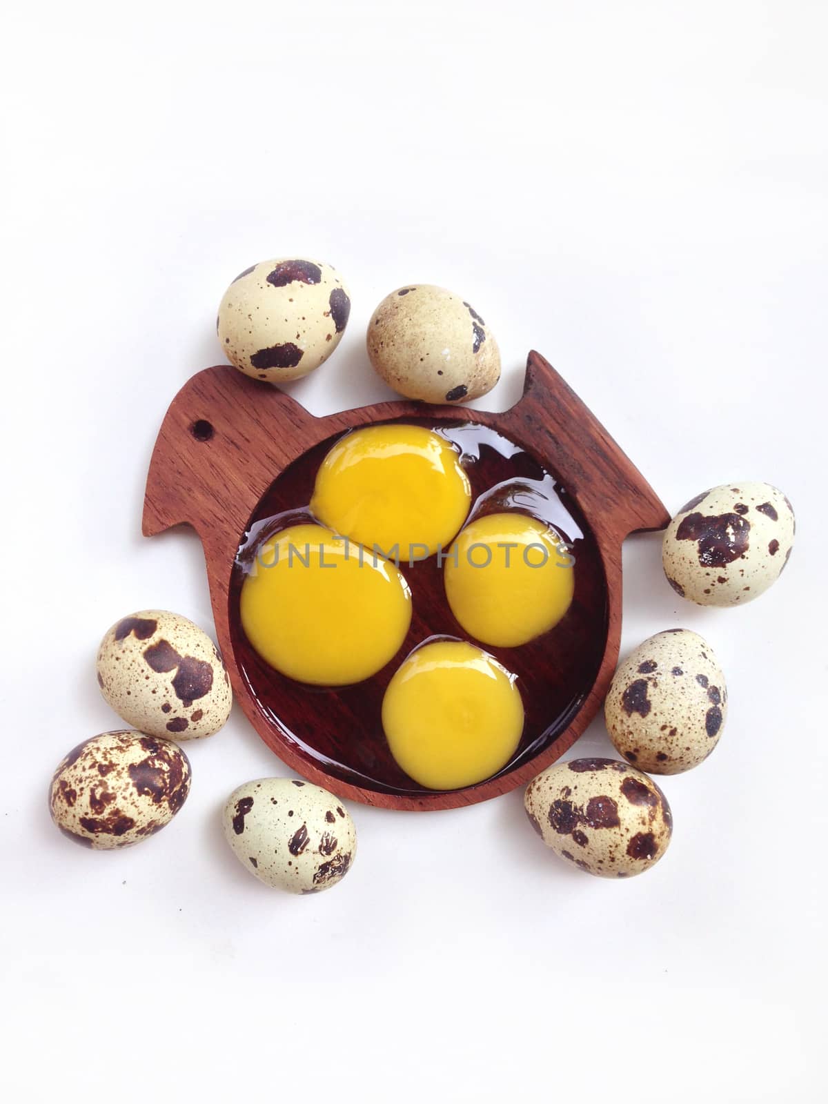 Quail eggs with yolk in wooden bird shaped saucer on white background