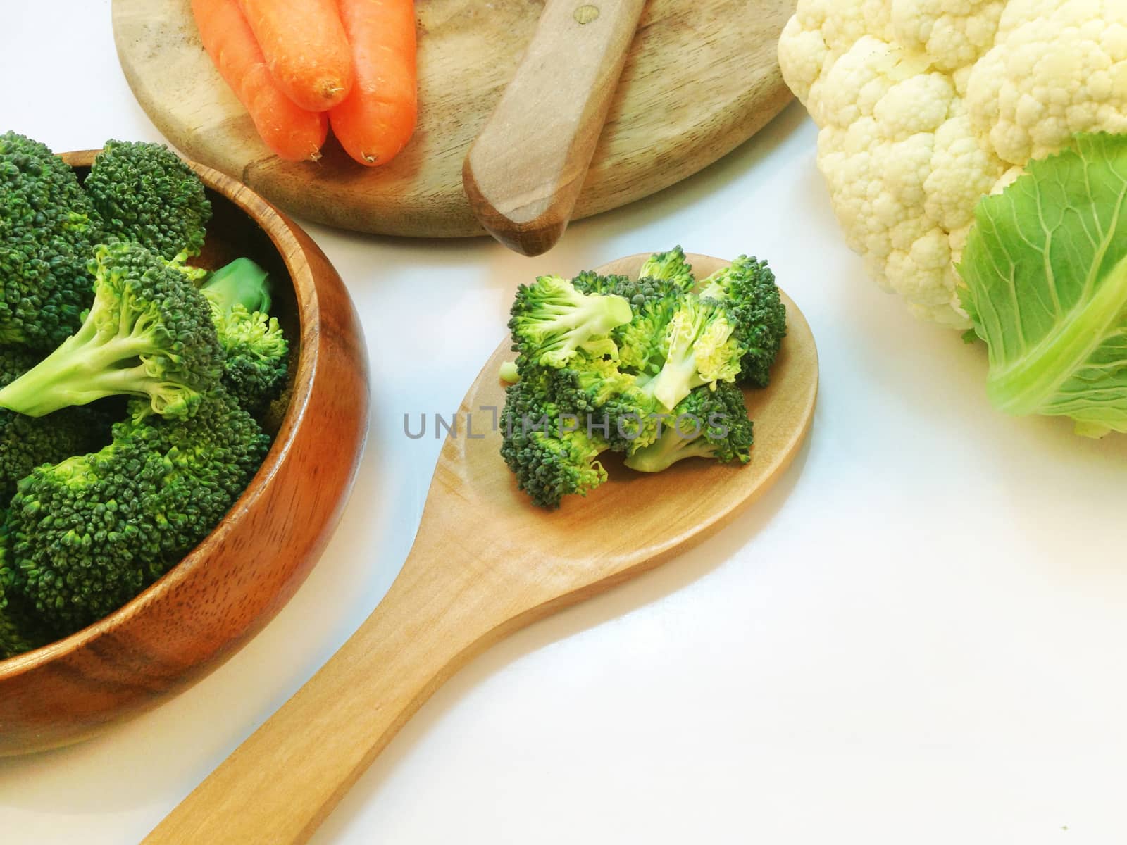 Broccoli in wooden bowl and wooden ladle with cauliflower on white background