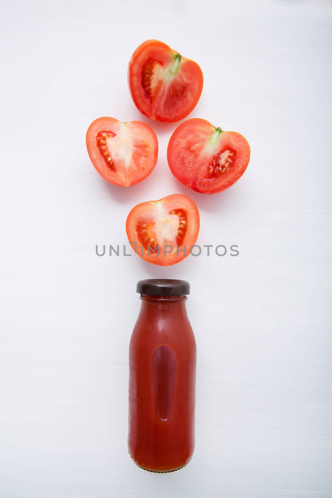 Tomatoes juice in bottle and fresh tomatoes slices on white wooden background.
