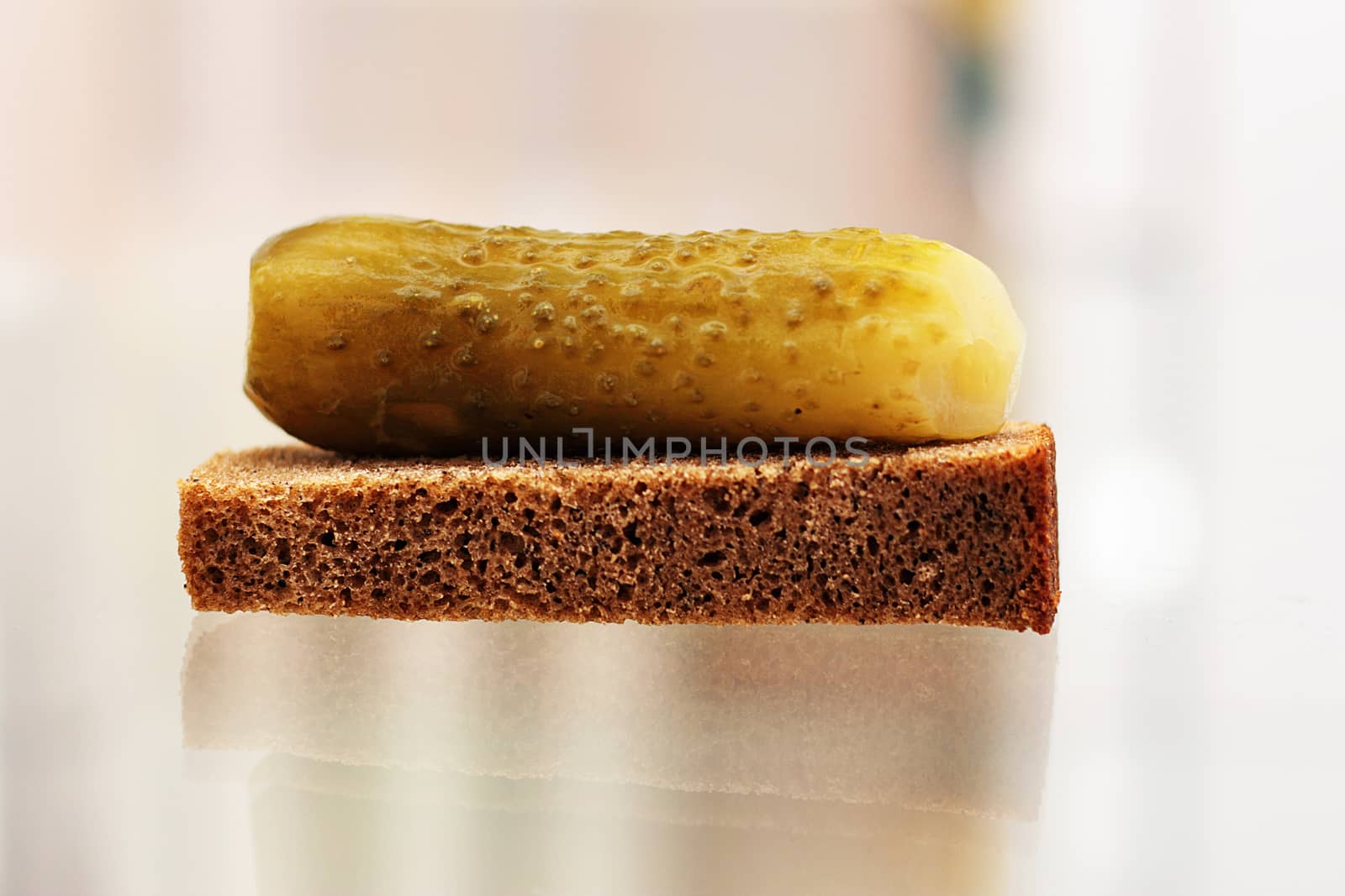 A piece of rye bread and a pickled cucumber on the kitchen glass table.