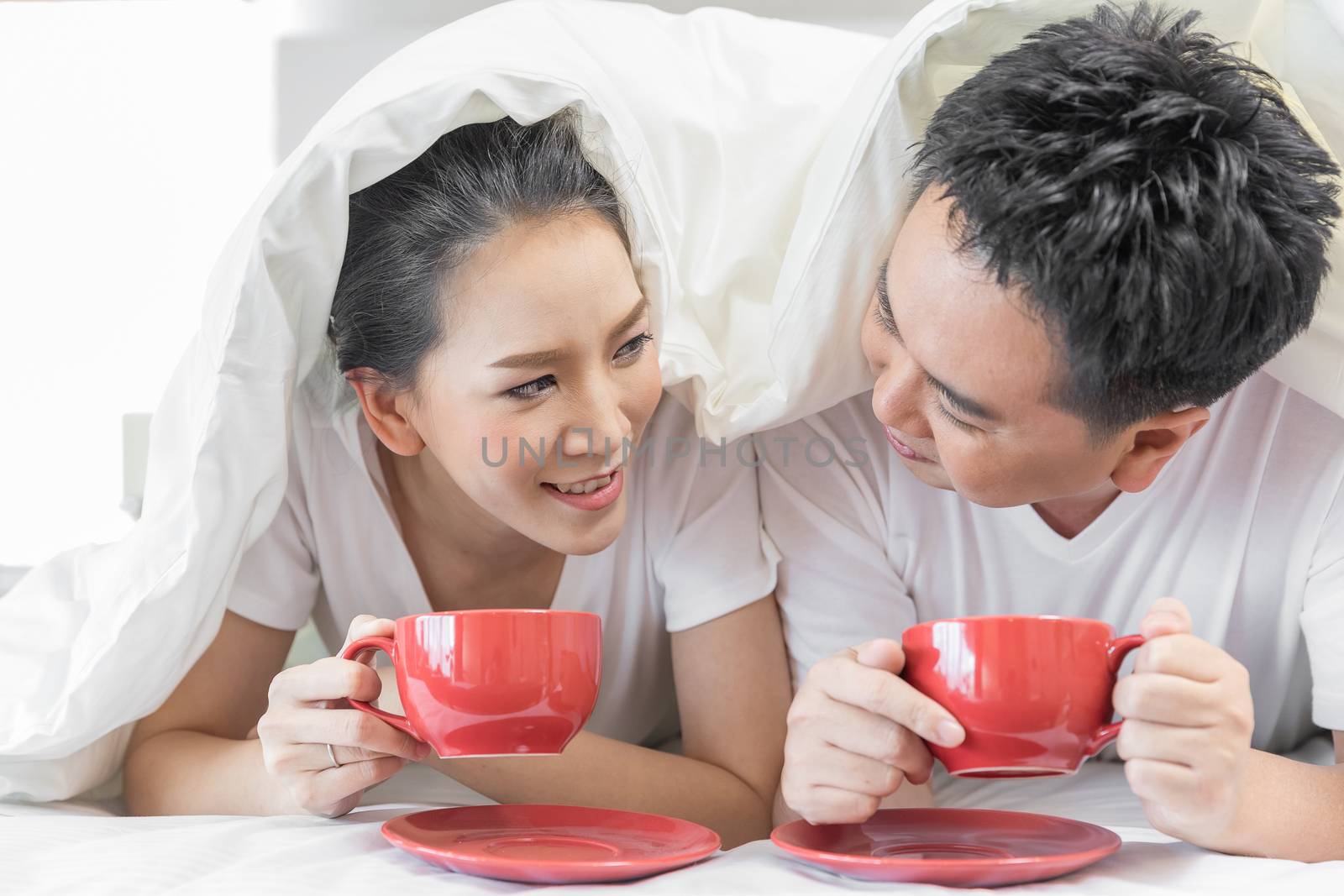 Young Asian Couples having breakfast on bed together in bedroom of contemporary house for modern lifestyle concept