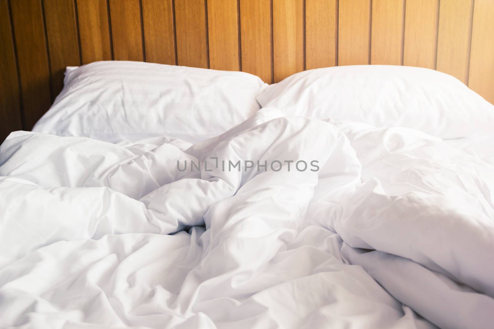 white pillow and blanket with wrinkle messy on bed in bedroom with lighting upper left side, from sleeping in a long night winter.