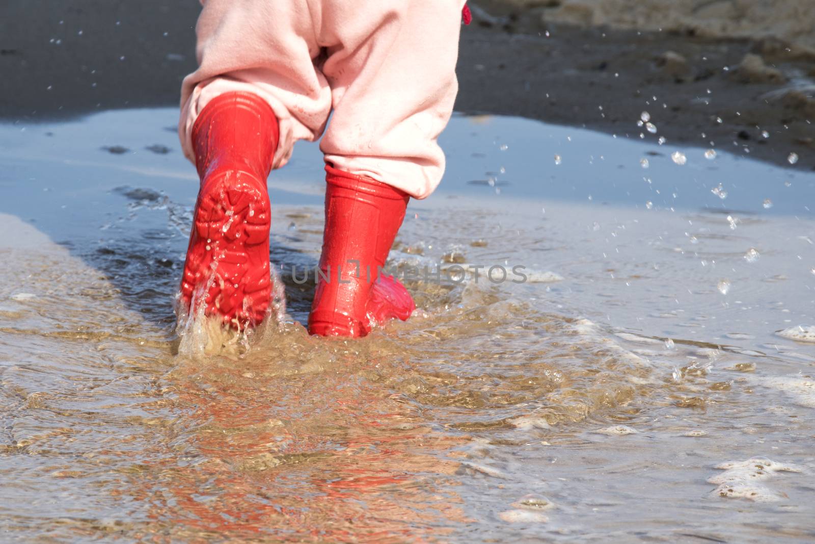 wellingtons in puddle.kid rubber boots in the sea background