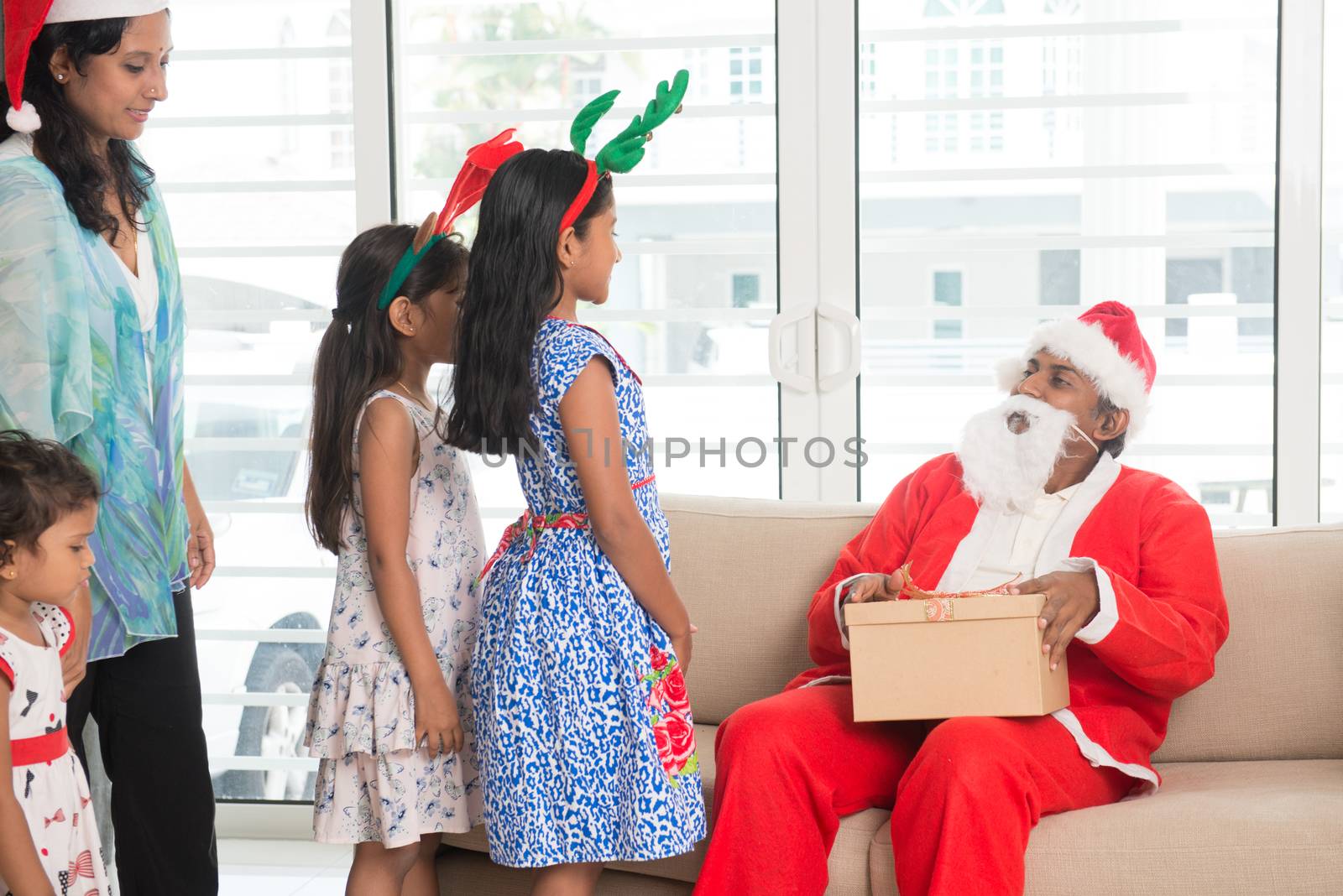 Happy Indian family celebrating Christmas holidays, with gift box and santa at home, Asian people festival mood indoors. 
