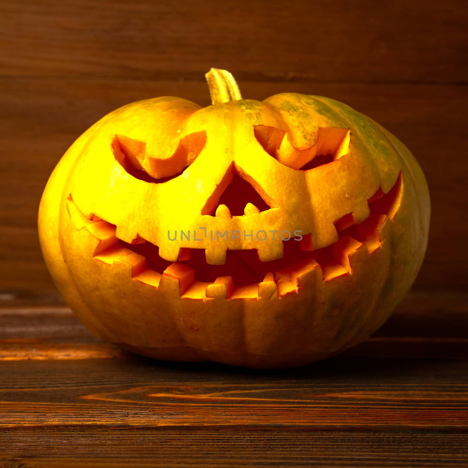 Scary Halloween pumpkin isolated on a wooden background . Scary glowing face trick or treat. Concept of halloween pumpkin on wooden planks. 