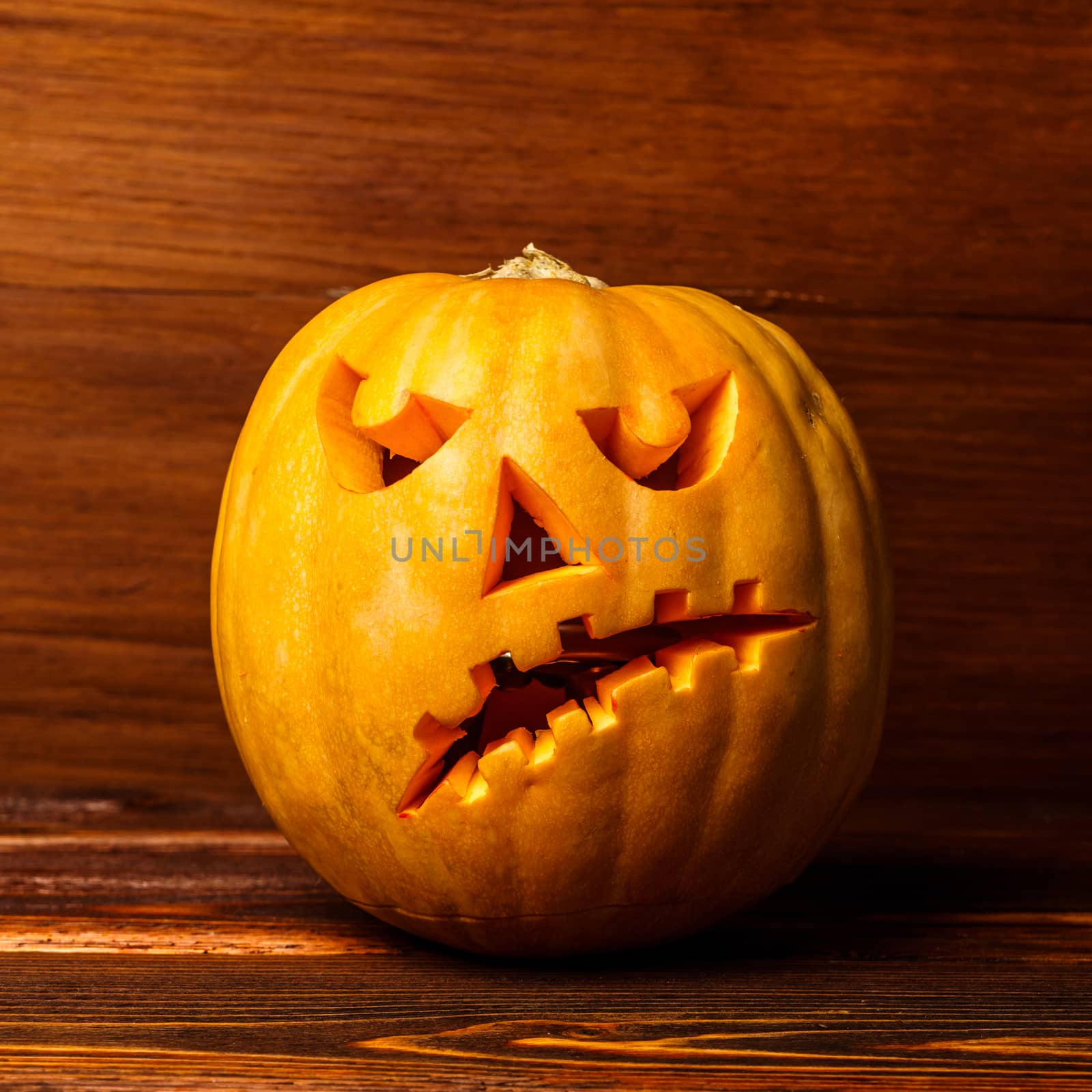 Scary Halloween pumpkin isolated on a wooden background . Scary glowing face trick or treat. Concept of halloween pumpkin on wooden planks. 