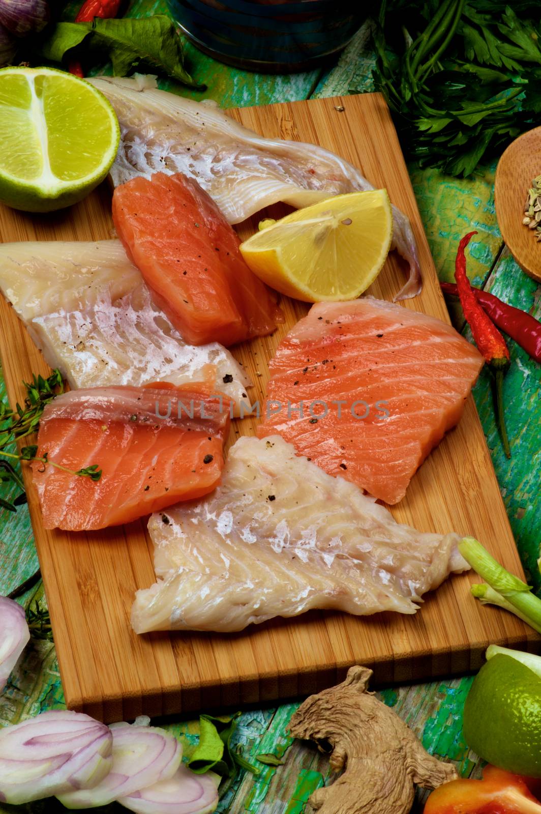 Arrangement of Raw Fillet of Salmon and Cod, Greens, Spices and Citrus Fruits closeup on Cracked Wooden background