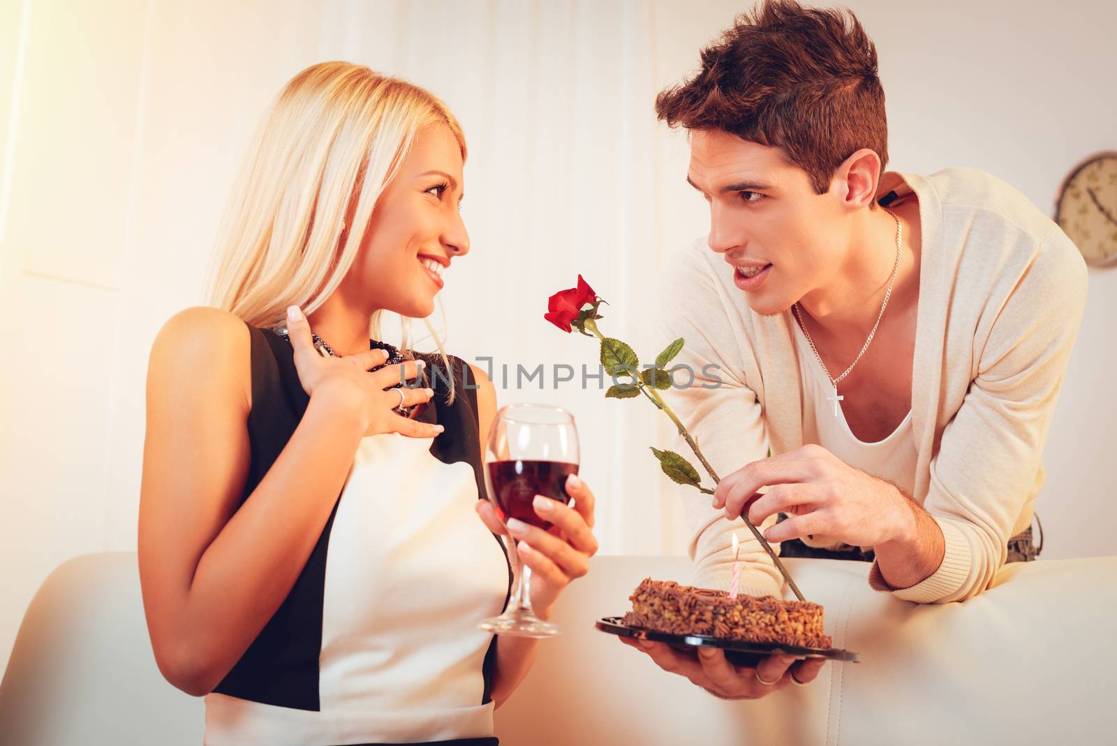 A young handsome man with a rose in his hand gives birthday cake to his beautiful surprised girl.