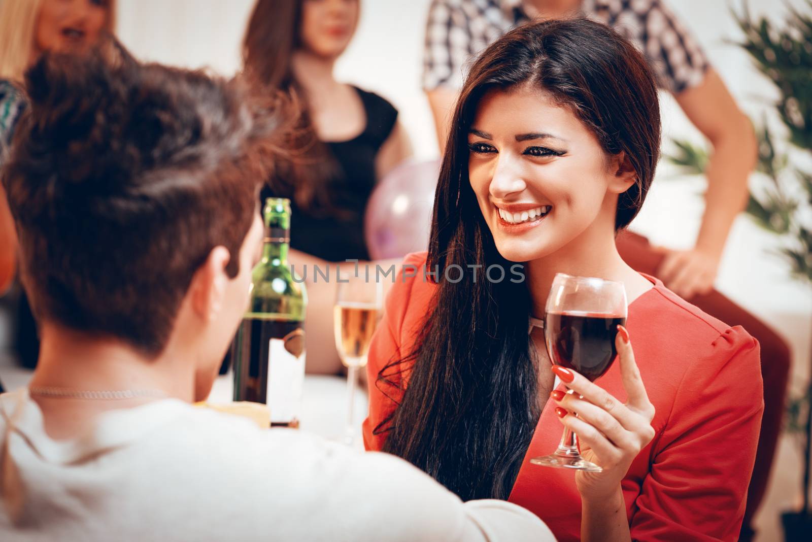 Young cute smiling girl holding a glass of wine on home party. She is looking at his boyfriend. Selective focus.