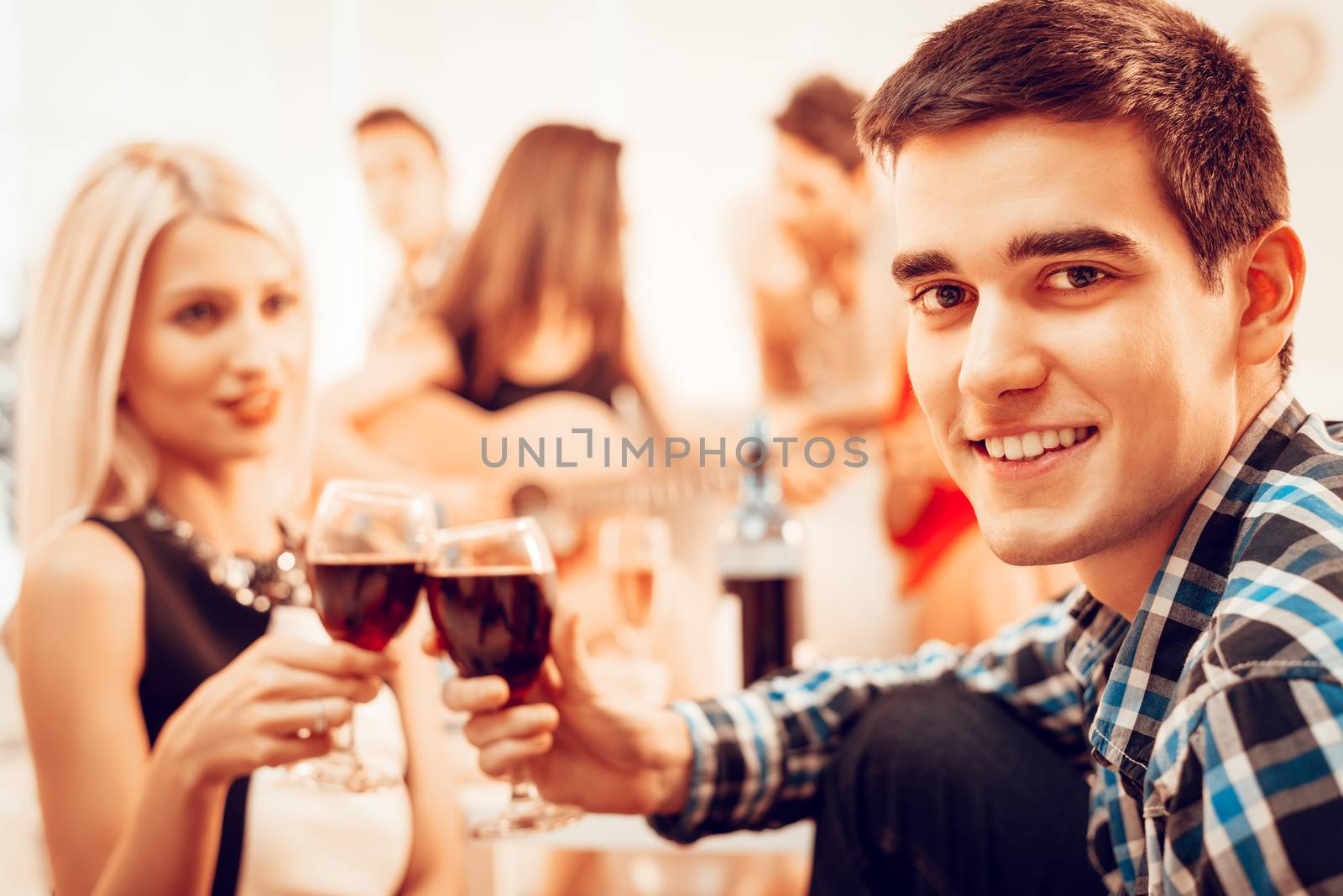 Handsome young man and his girlfriend toasting with red wine at the house party. Selective focus. Focus on guy. He is looking at camera.